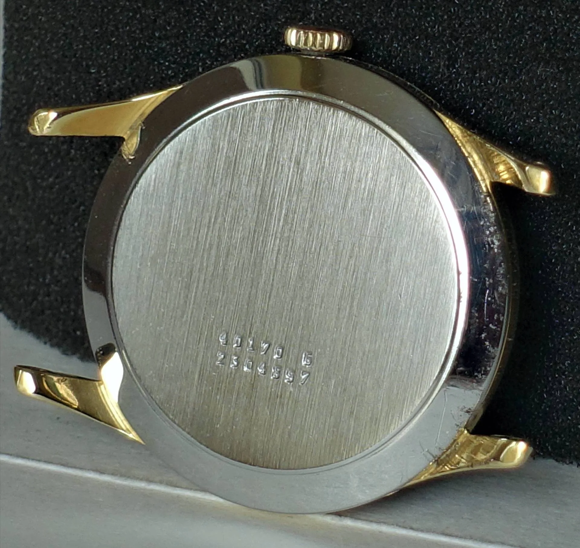 Rundes Uhrengehäuse mit silberfarbener Rückseite und goldfarbenen Hörnern und Krone.