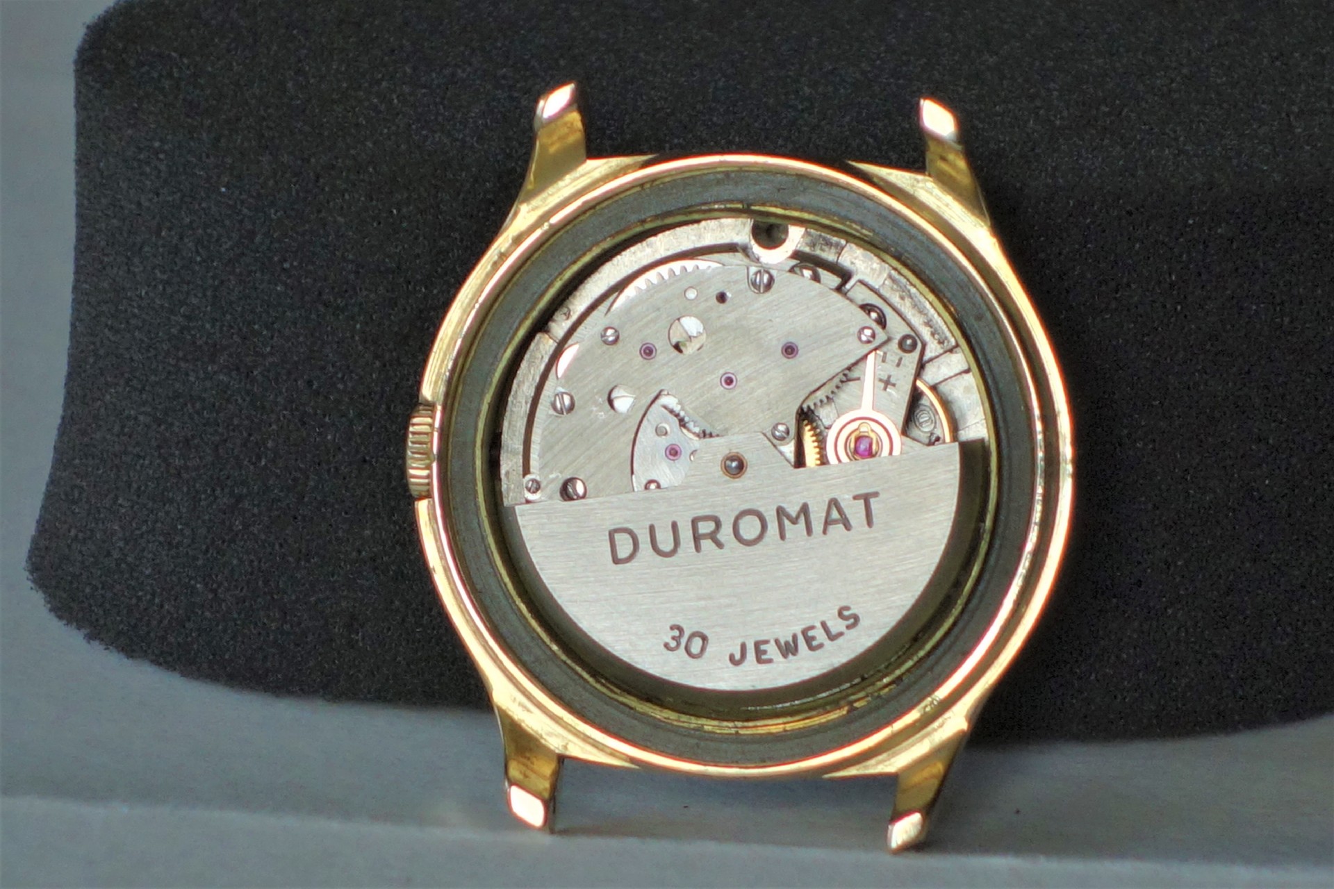 Silberfarbenes Uhrwerk mit der Aufschrift "DUROMAT 30 JEWELS" in einem goldfarbenen Uhrengehäuse.