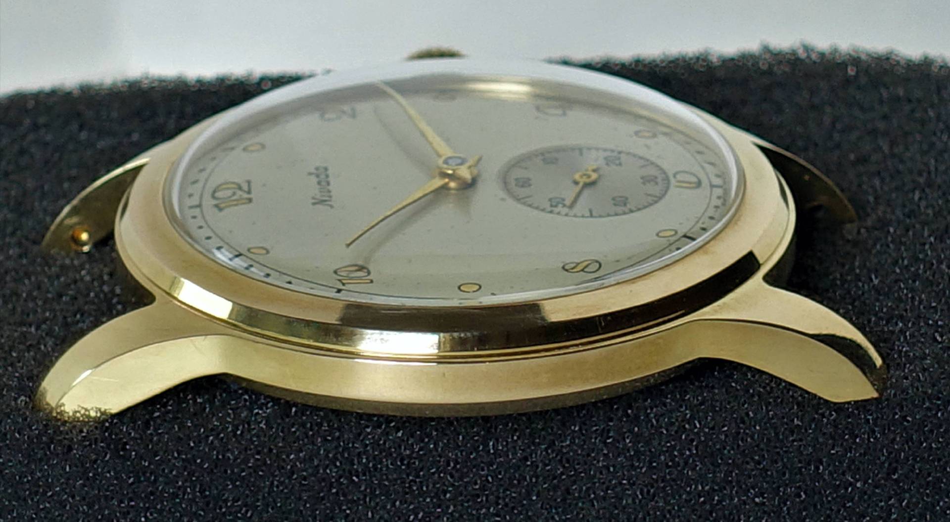 Flache Armbanduhr mit goldfarbenem Gehäuse und hellem Zifferblatt.