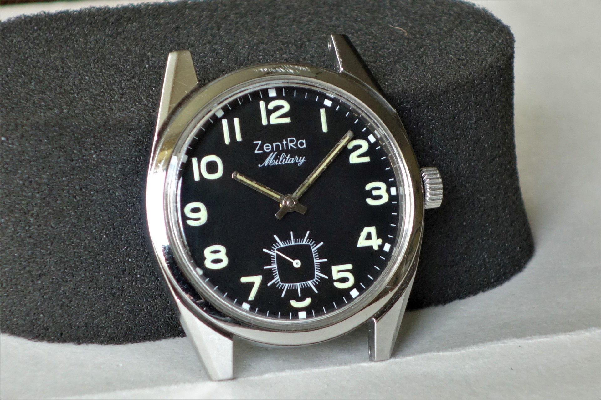 Schwarze Armbanduhr mit Leuchtziffern und silberfarbenem Gehäuse.