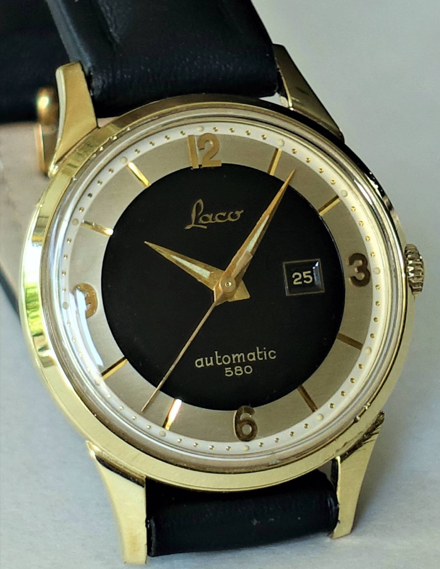 Goldfarbene Armbanduhr mit schwarzem Zifferblatt, Datumsanzeige und schwarzem Armband.