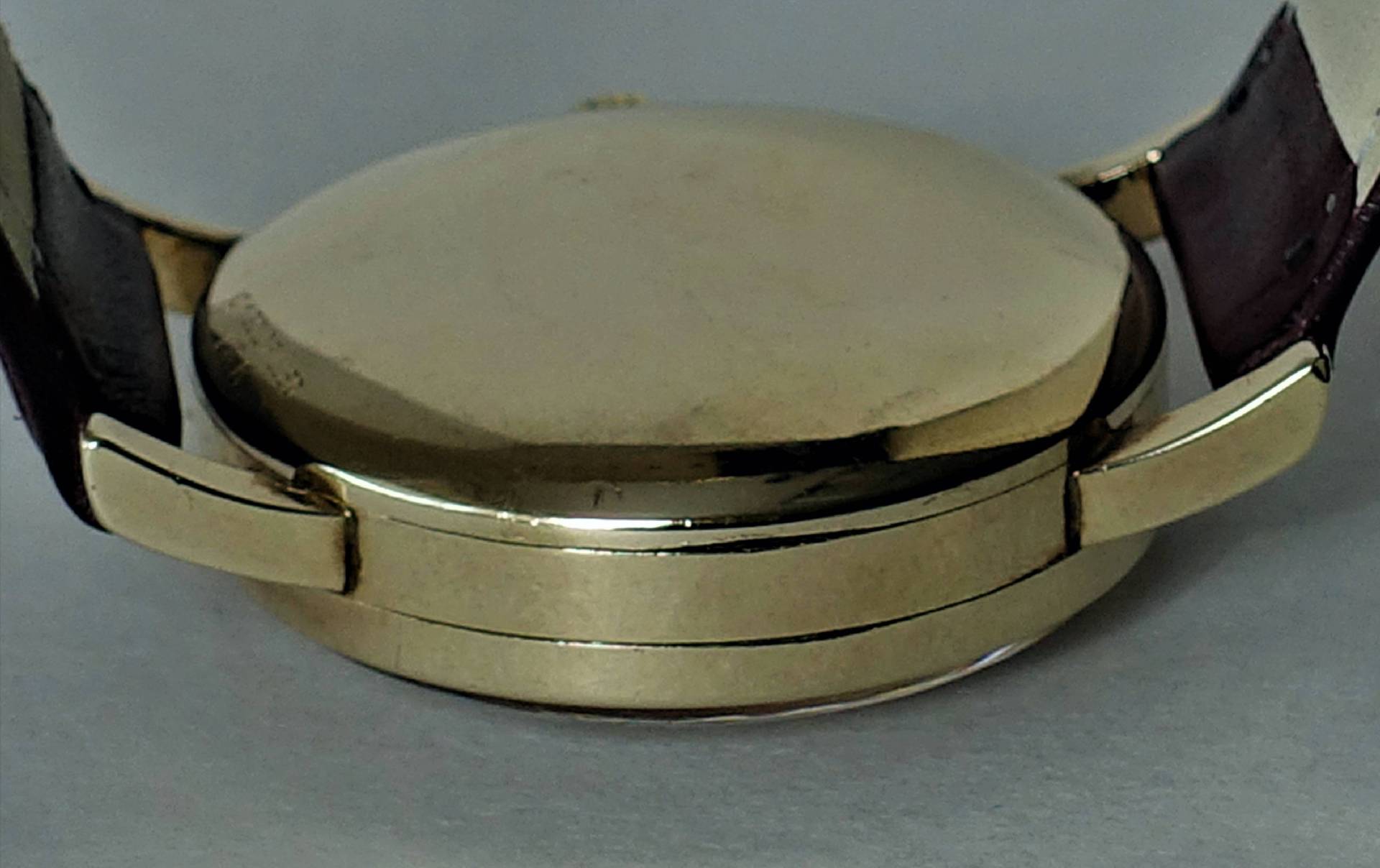 Detailansicht einer eleganten Armbanduhr mit goldfarbenem Gehäuse und Lederarmband