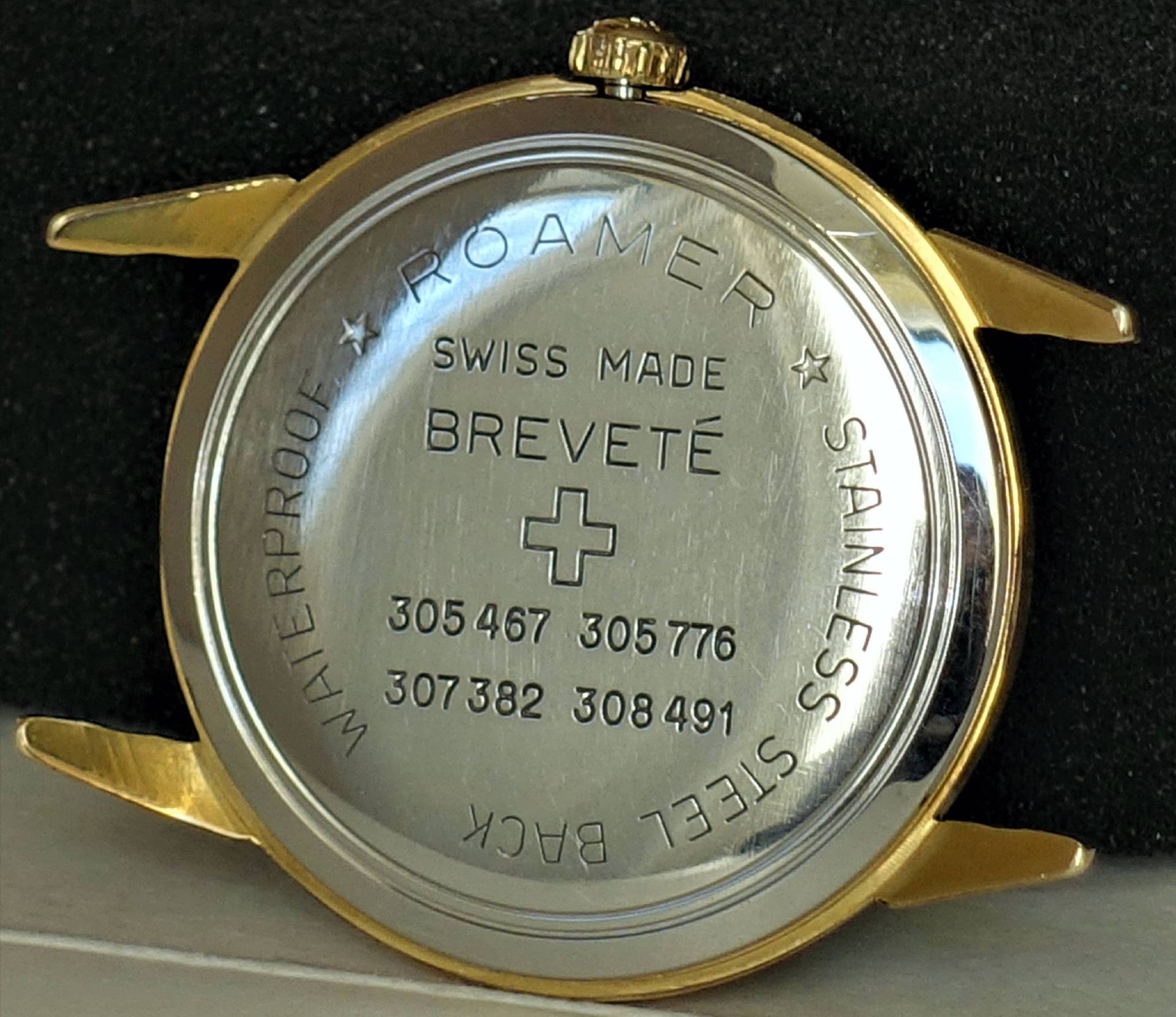 Zweifarbiges Uhrgehäuse mit silberner Rückseite und goldfarbenem Rand, Gravur und Krone oben.