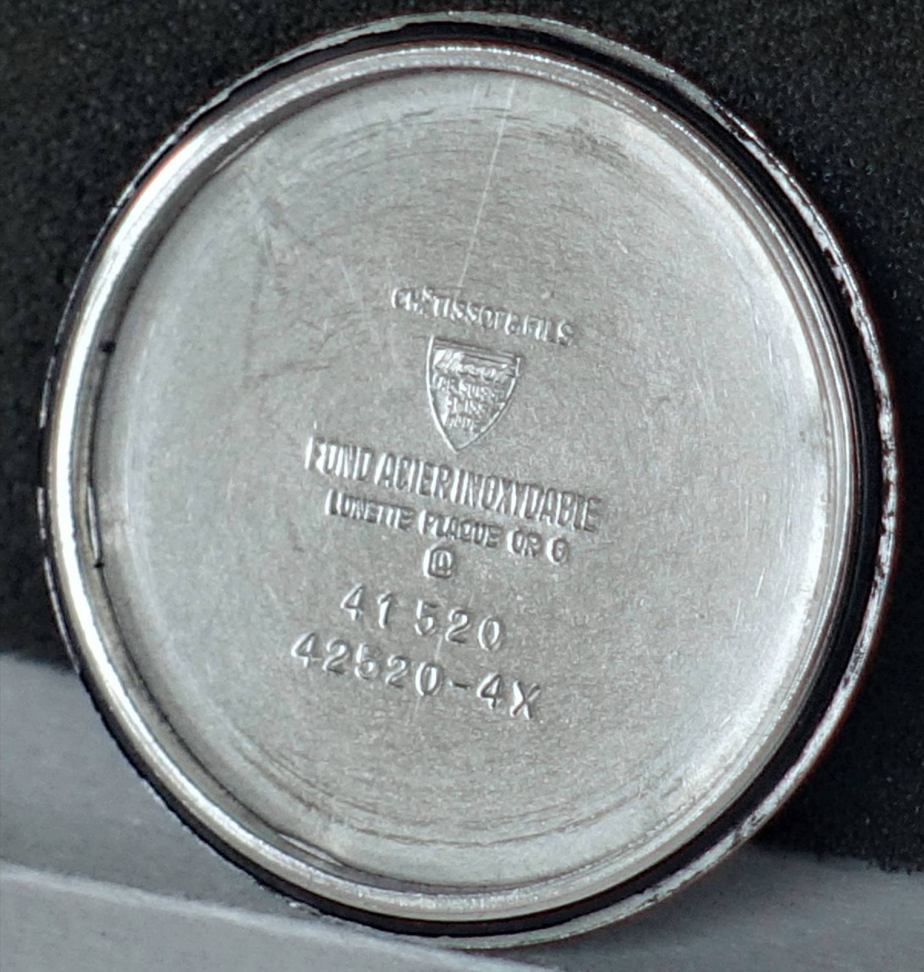 Runder silberfarbener Gehäuseboden für eine Armbanduhr mit eingravierten Zahlen und Schriftzügen.