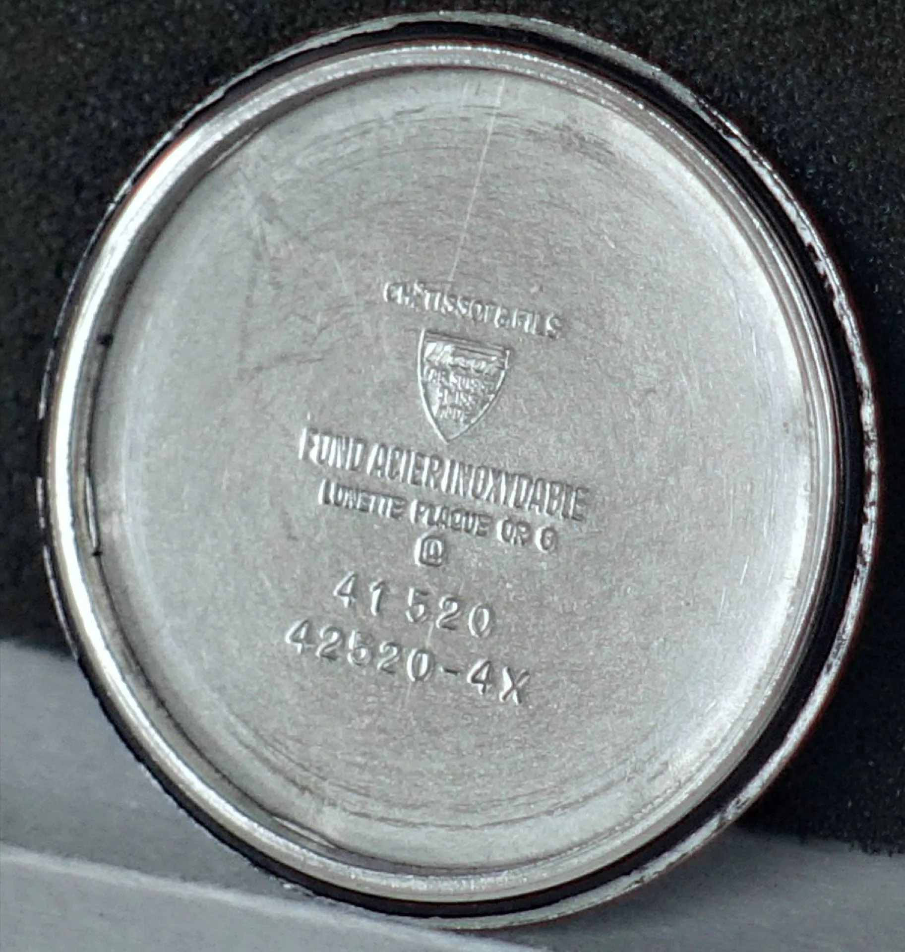 Runder silberfarbener Gehäuseboden für eine Armbanduhr mit eingravierten Zahlen und Schriftzügen.