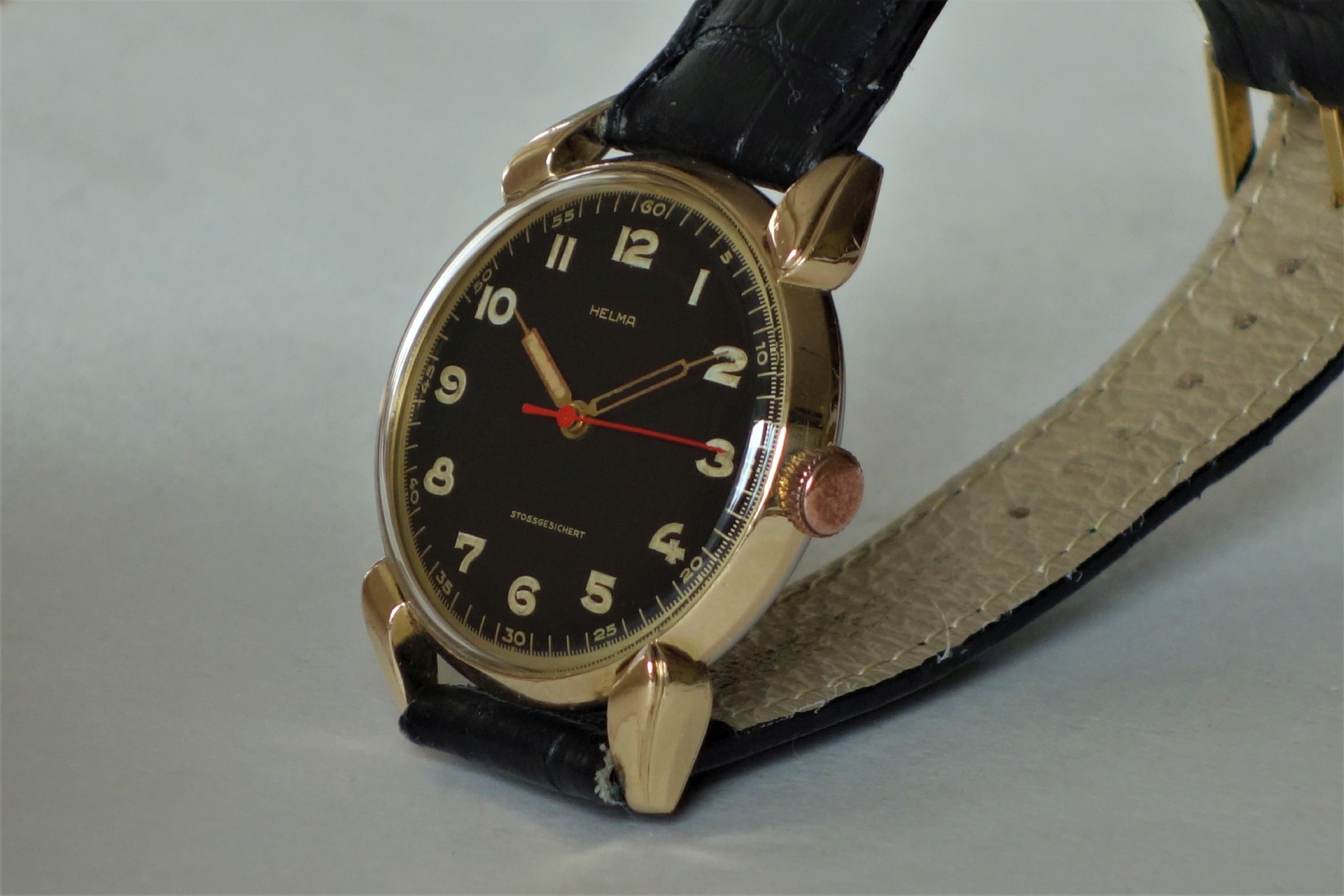 Analoge Armbanduhr mit schwarzem Zifferblatt, goldfarbenem Gehäuse und schwarzem Armband.