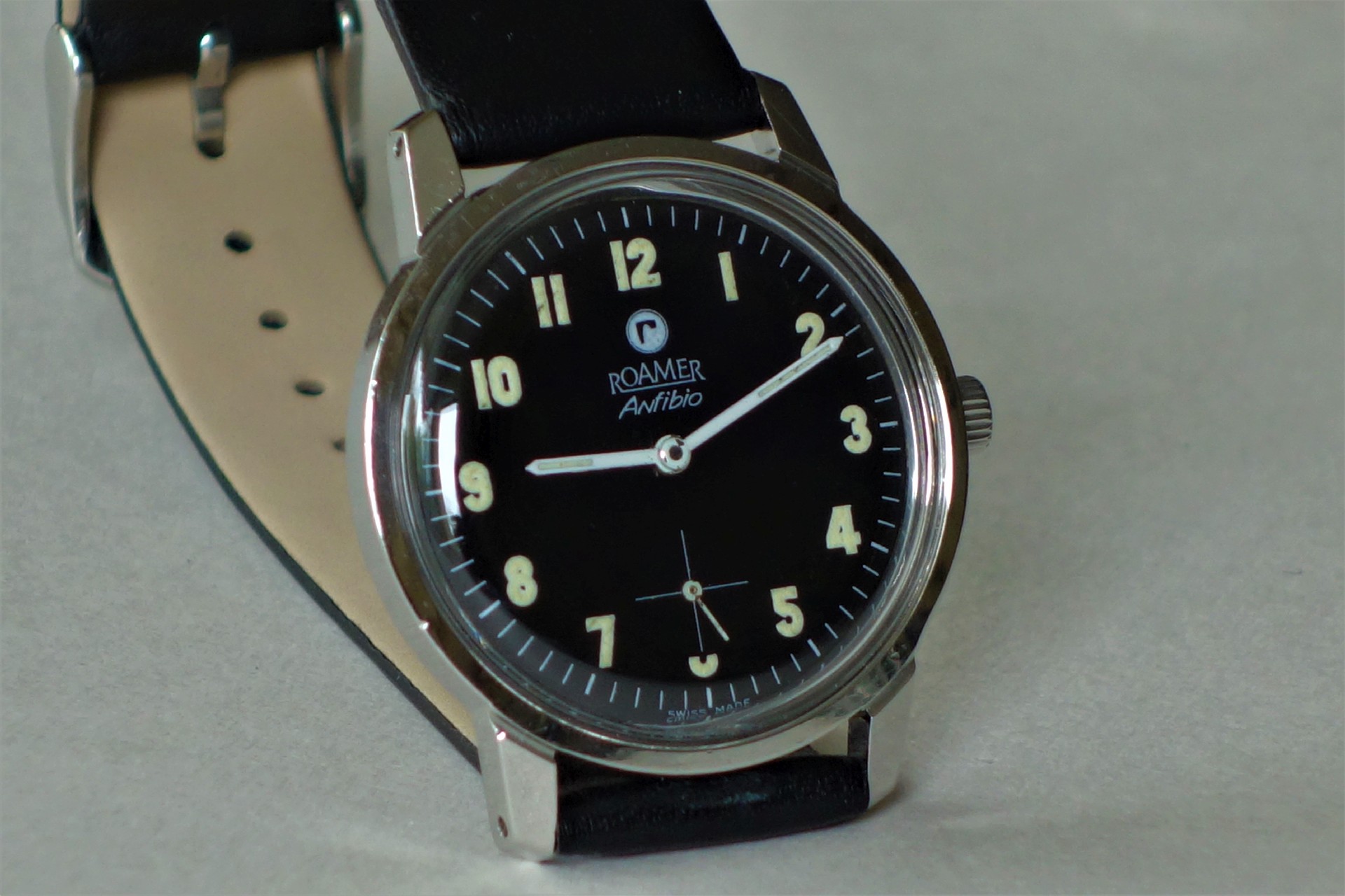 Schwarze Armbanduhr mit hellem Zifferblatt, silberfarbenem Gehäuse und schwarzem Armband.