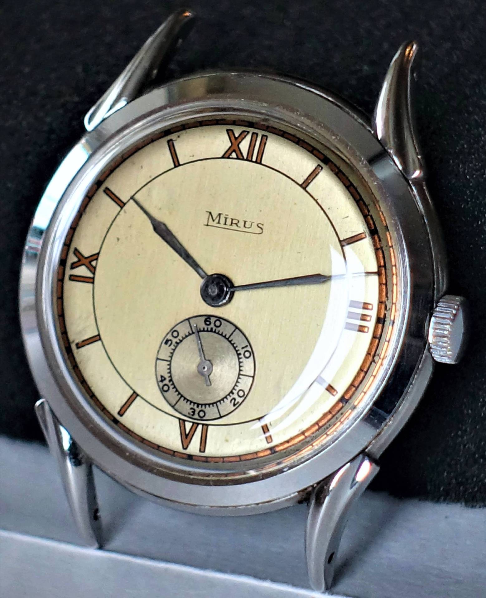 Runde Armbanduhr mit beigem Zifferblatt, römischen Zahlen und silberfarbenem Gehäuse.