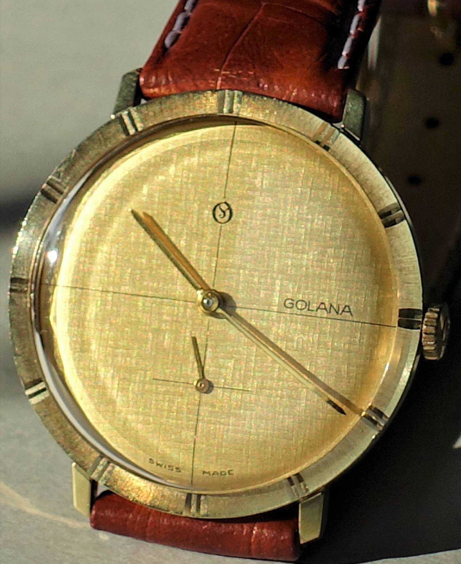 Goldfarbene Armbanduhr mit braunem Armband und schlichtem Zifferblatt.