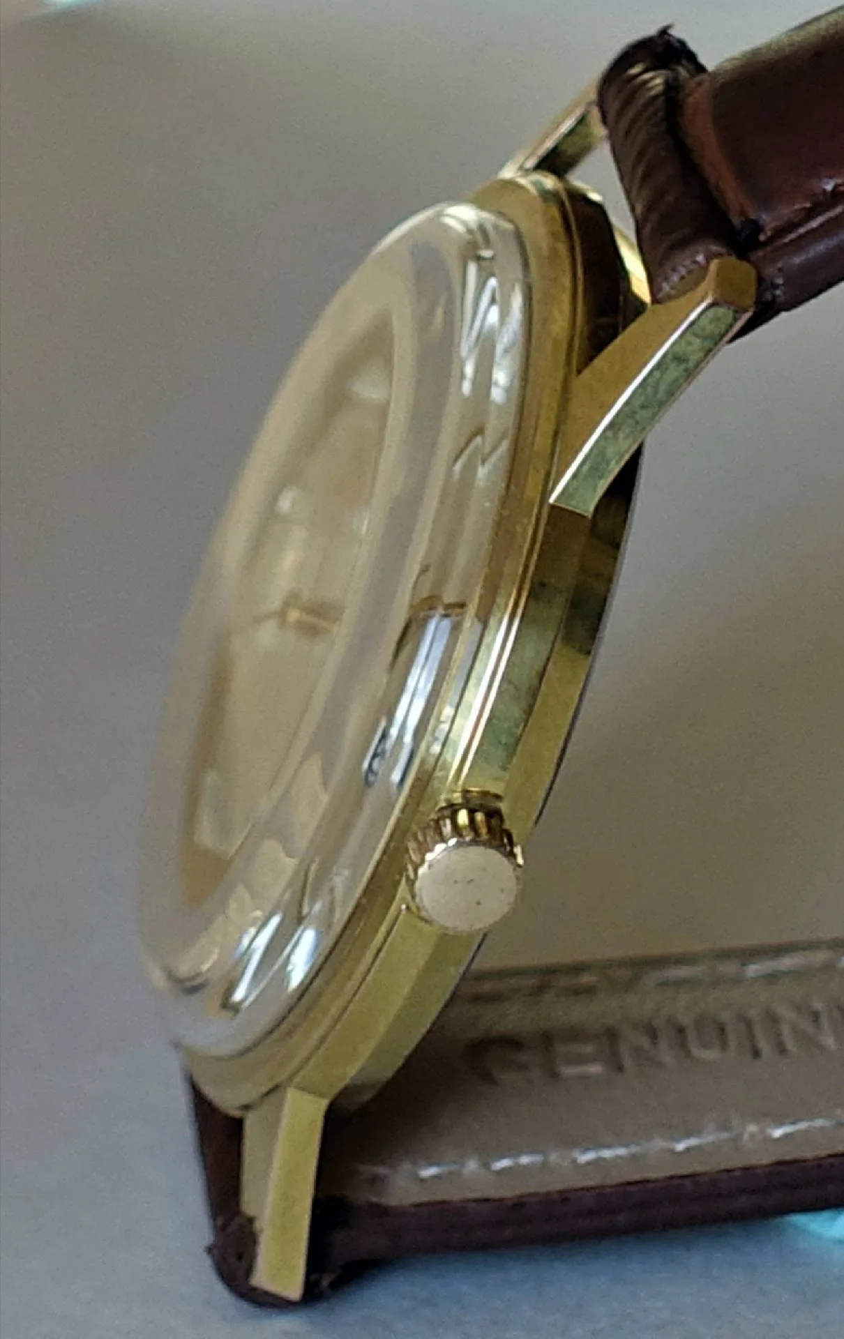 Seitliche Nahaufnahme einer Armbanduhr mit gelbfarbenem Gehäuse, gewölbtem Glas und braunem Lederarmband.