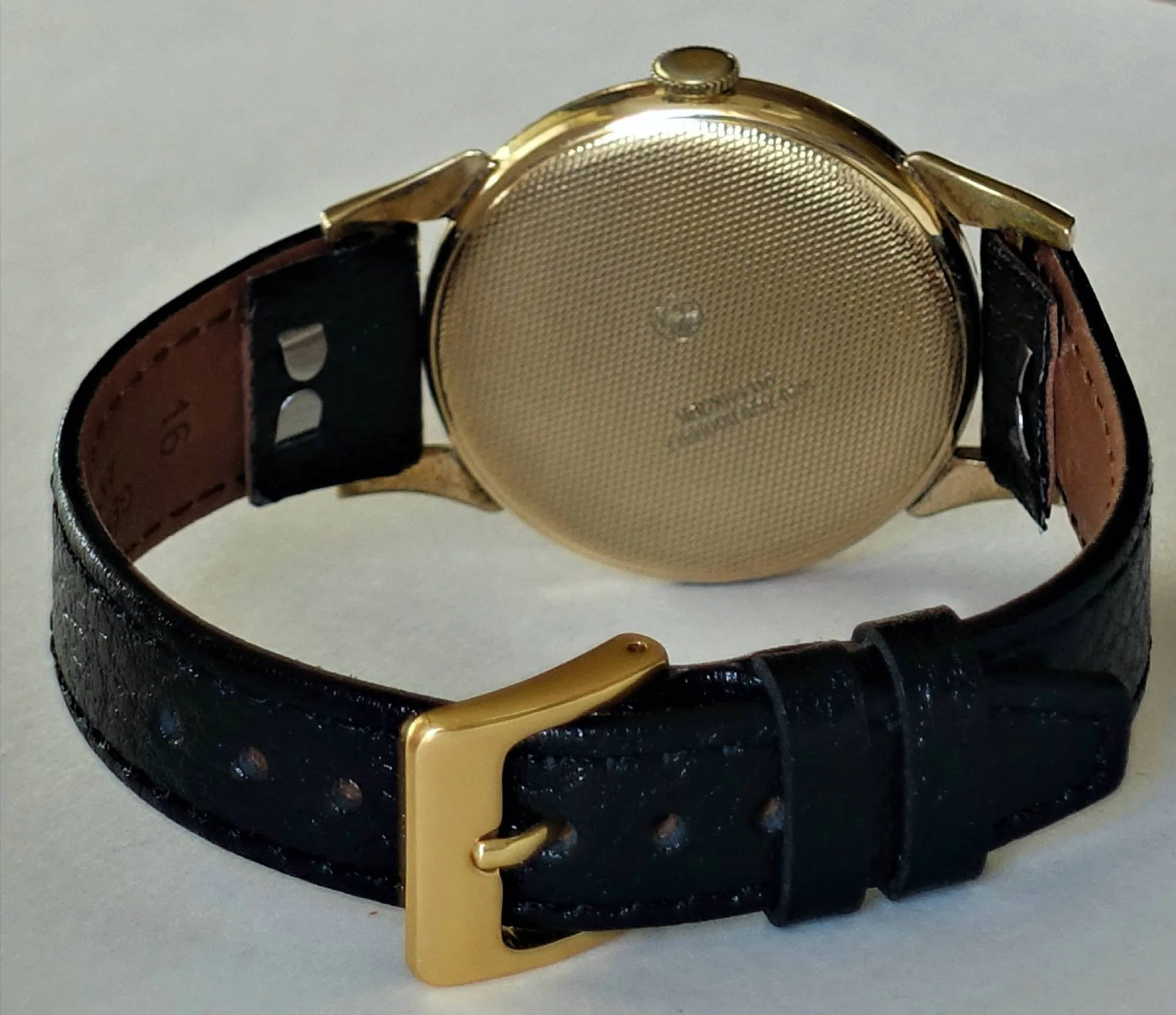 Runde gelbe Uhr, schwarzes Lederarmband, Rückansicht Eine runde Uhr mit gelbem Gehäuse und schwarzem Lederarmband ist von hinten zu sehen.
