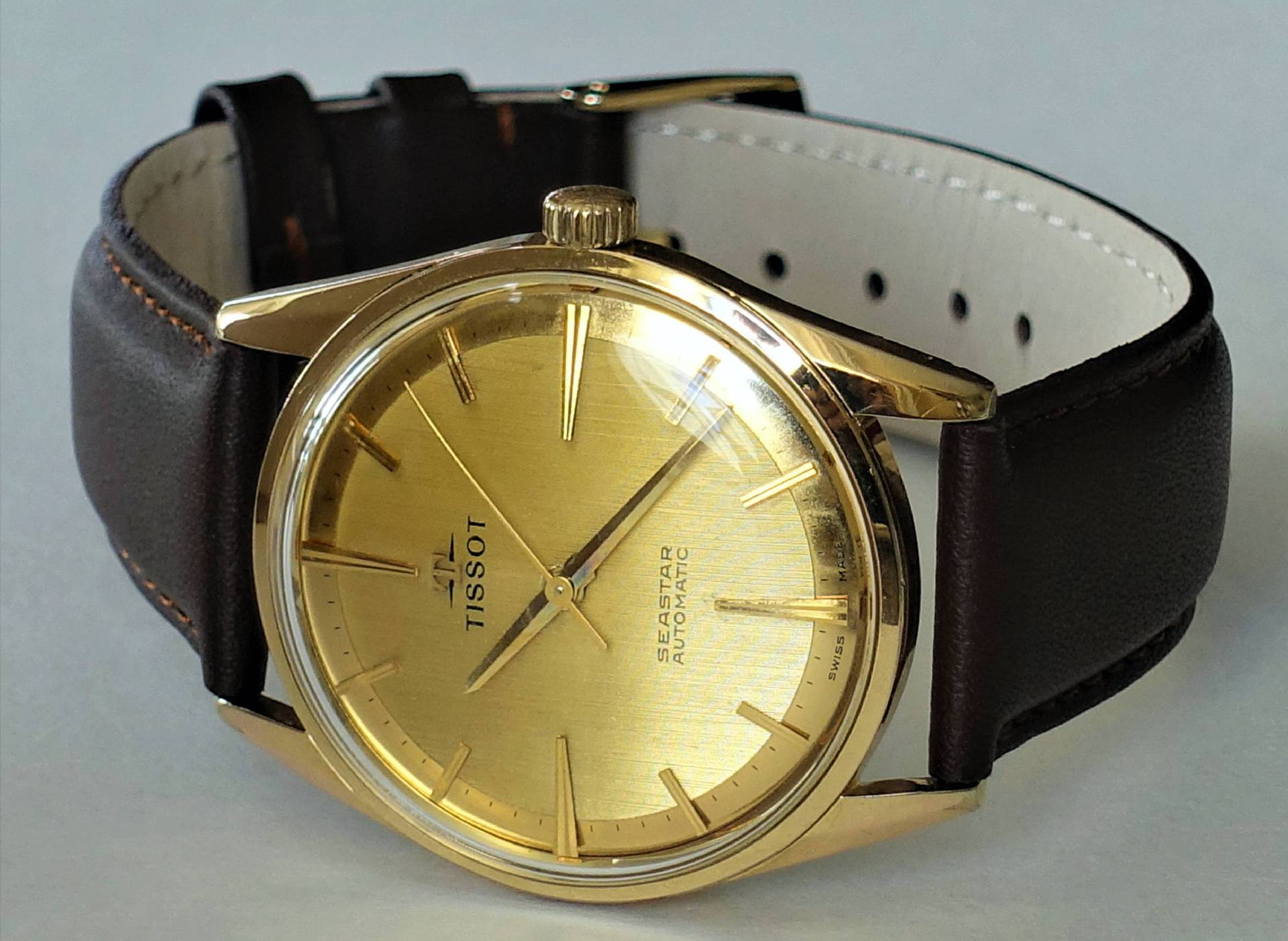 Goldfarbene Armbanduhr mit braunem Armband und goldfarbenem Zifferblatt, Modell Tissot Seastar Automatic.