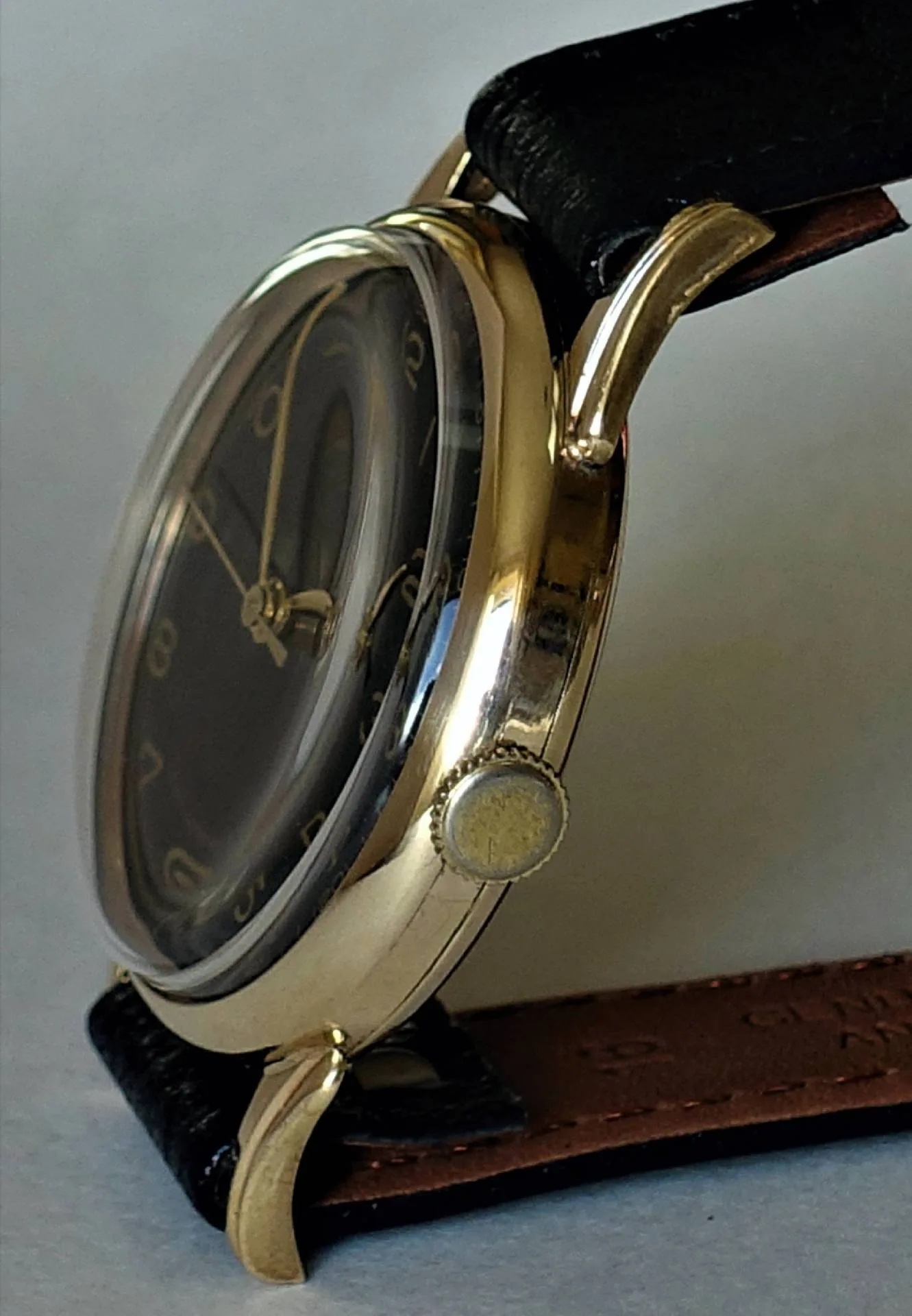 Schwarzes Zifferblatt goldfarbenes Gehäuse Seitliche Nahaufnahme einer Armbanduhr mit schwarzem Zifferblatt, goldfarbenem Gehäuse und schwarzem Armband.