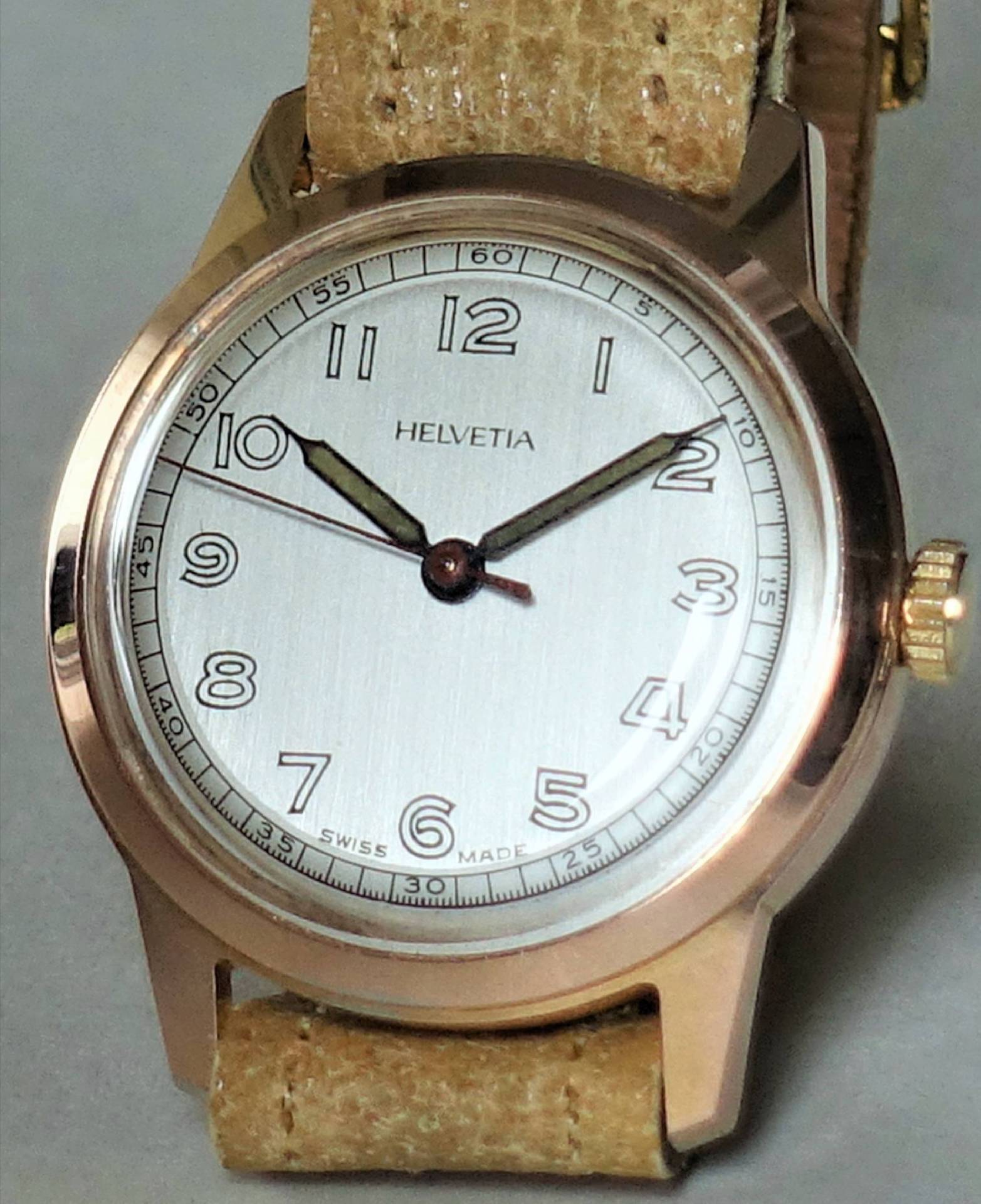 Runde Armbanduhr mit beigem Lederarmband und hellem Zifferblatt, Aufschrift "Helvetia".