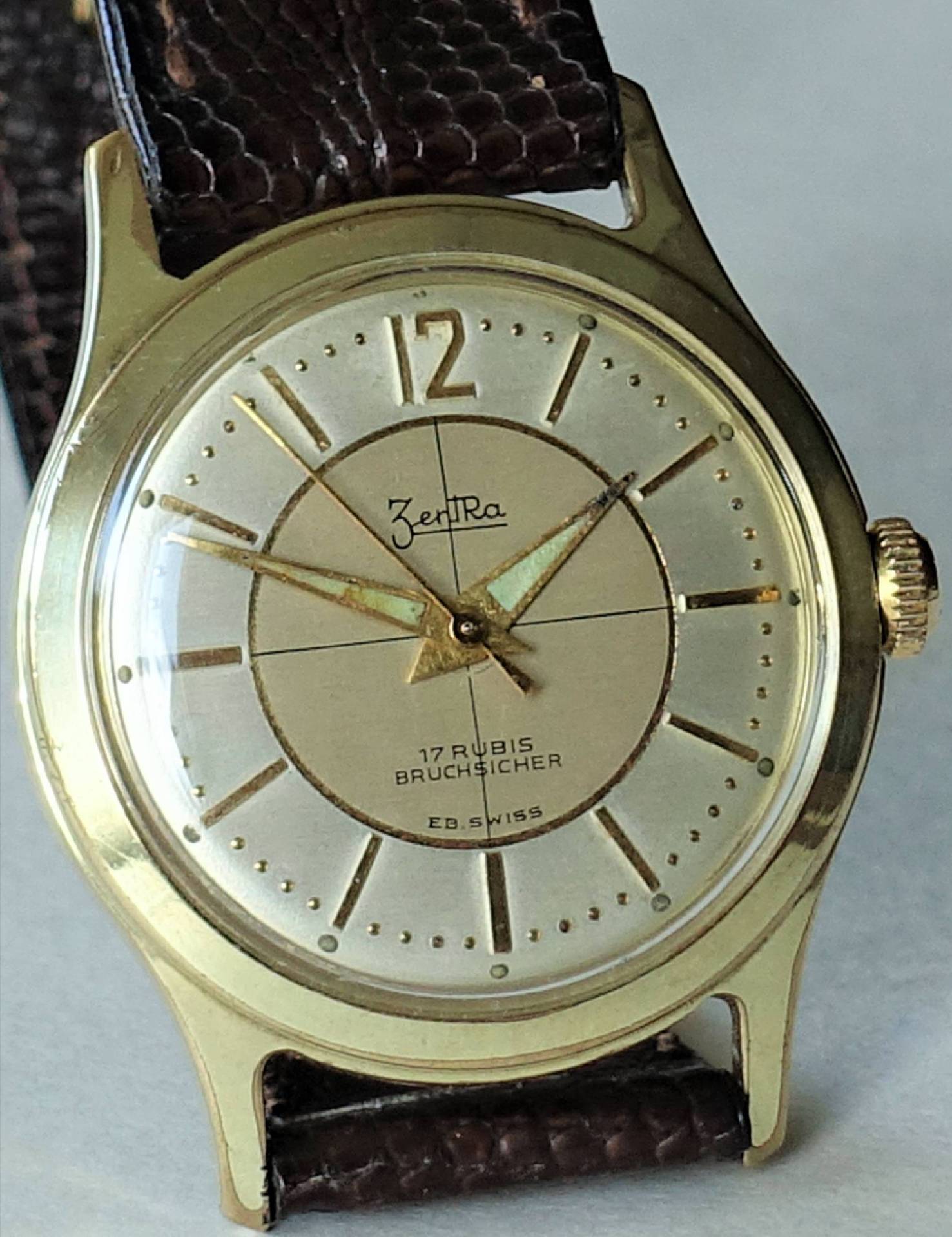 Goldfarbene Armbanduhr mit hellem Zifferblatt und braunem Armband.