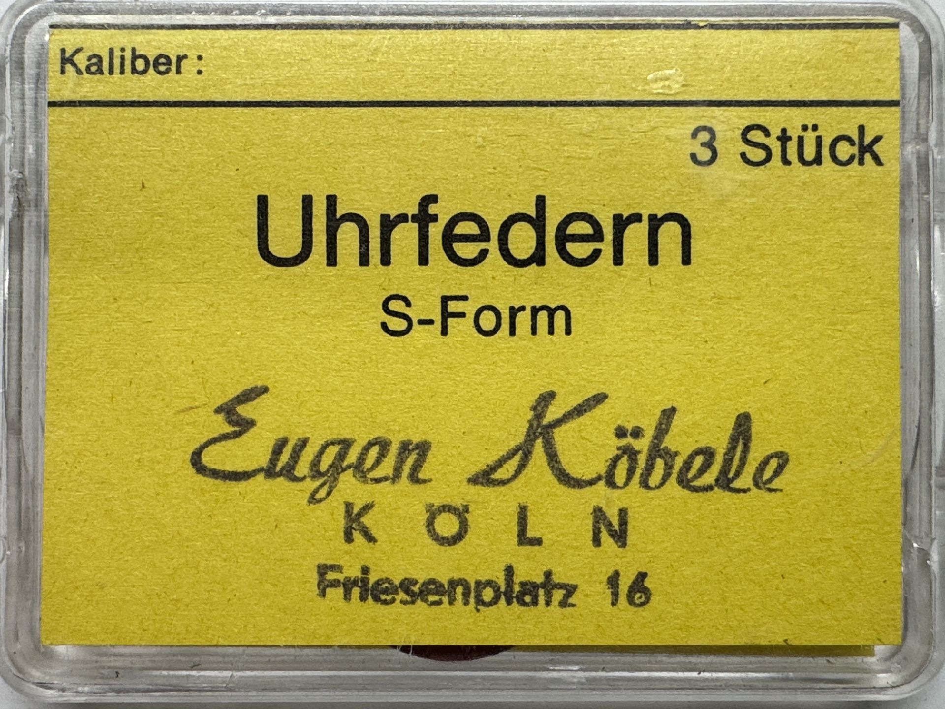Gelbe Verpackung mit drei S-förmigen Uhrfedern als Ersatzteile.