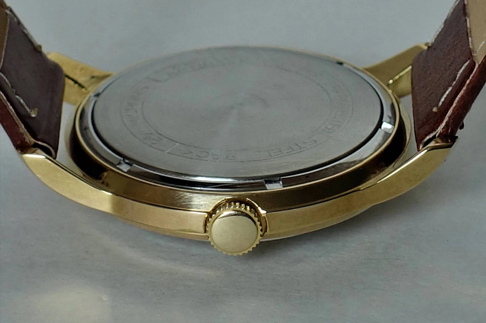 Armbanduhr Rückseite goldfarben Rückseite einer goldfarbenen Armbanduhr mit braunem Armband und silberfarbenem Gehäuseboden.