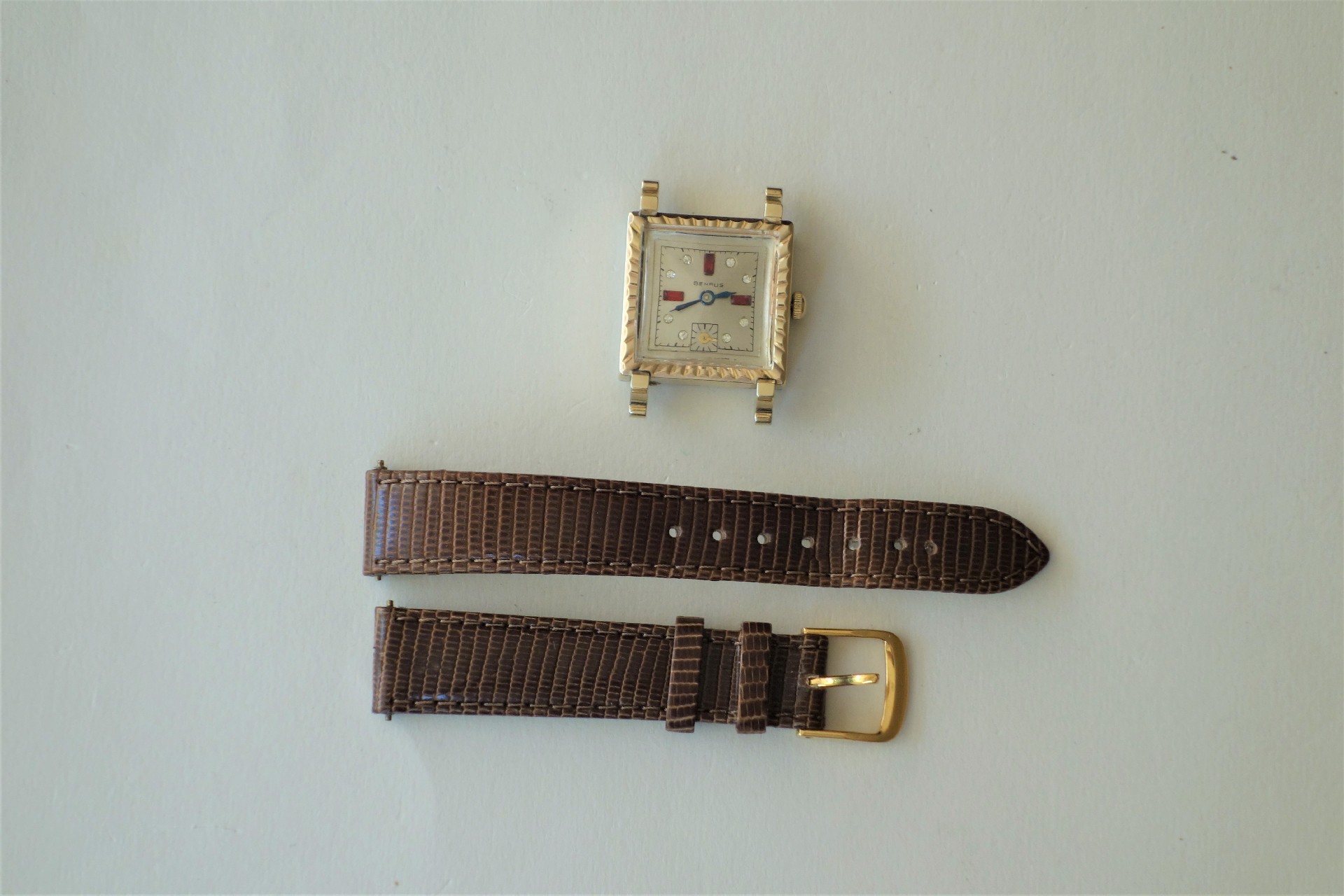 Zerlegte quadratische Damenuhr mit goldfarbenem Gehäuse und braunem Lederarmband.