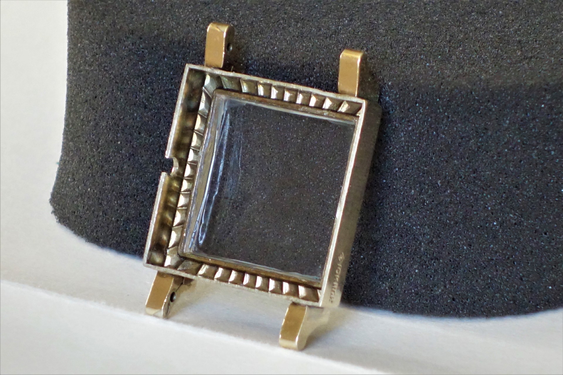 Eckiges Uhrengehäuse aus Metall mit Glasabdeckung.