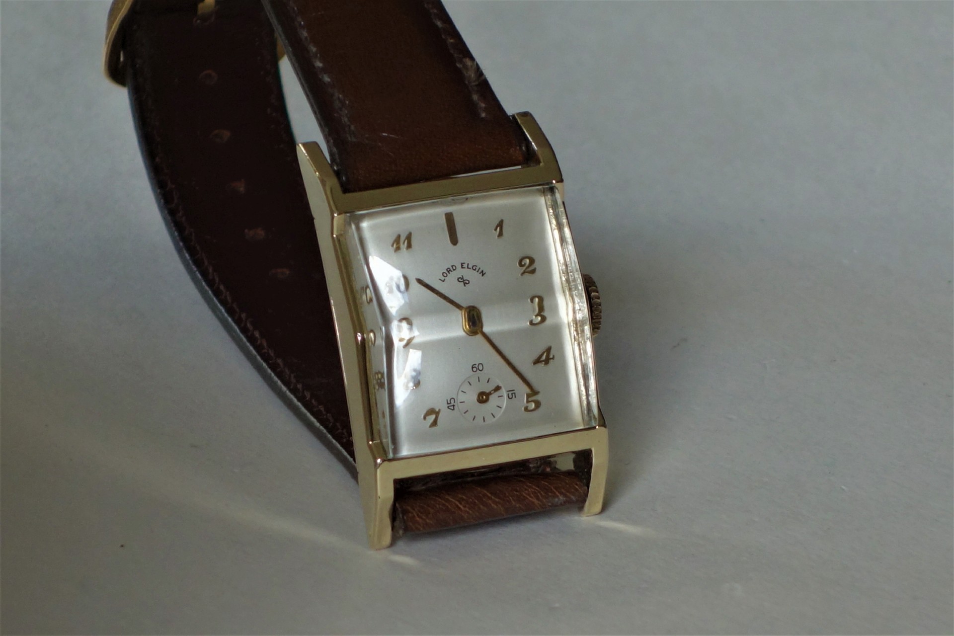 Rechteckige Armbanduhr mit hellem Zifferblatt und braunem Armband.