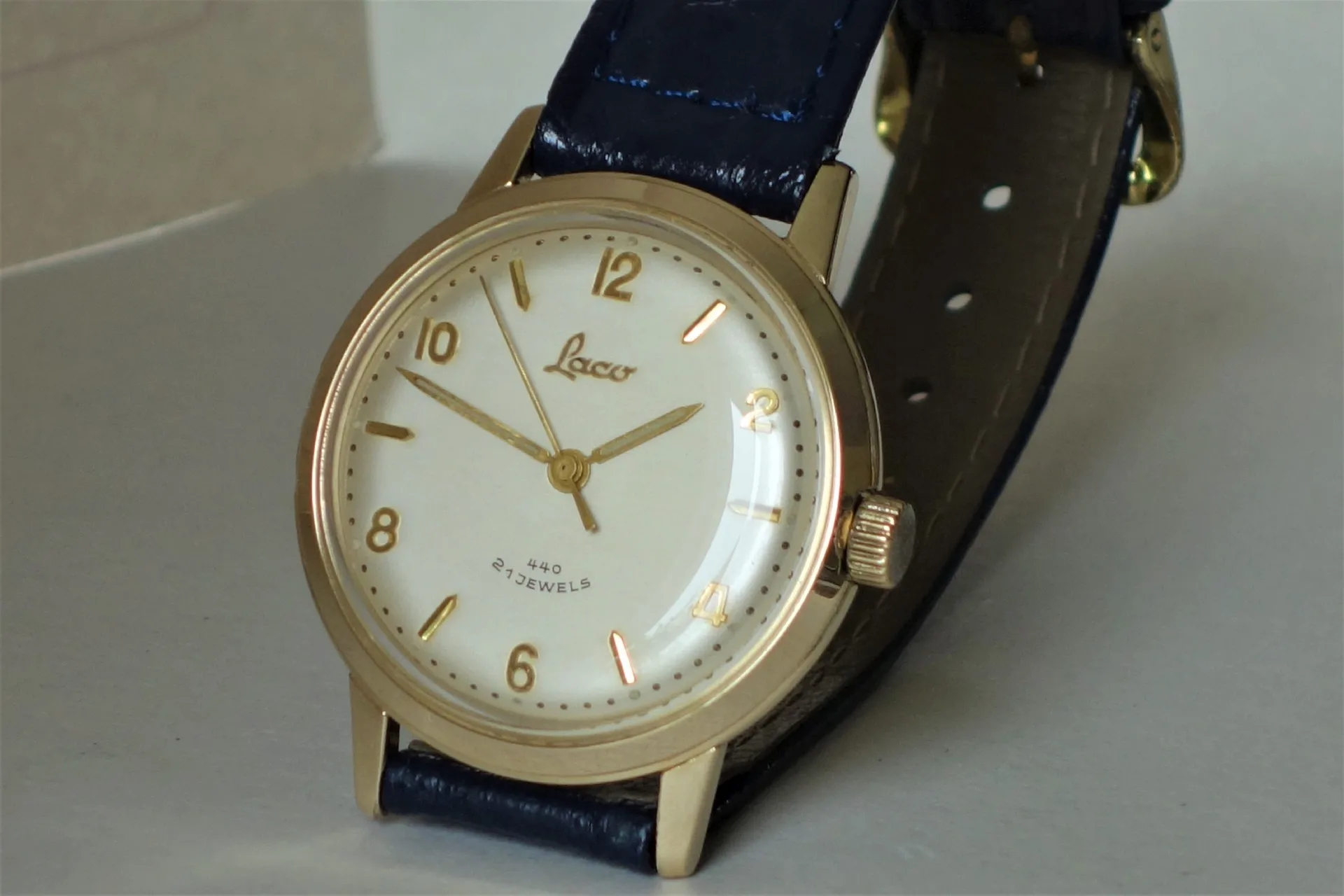 Analoge Armbanduhr mit goldfarbenem Gehäuse, weißem Zifferblatt und dunkelblauem Lederarmband.