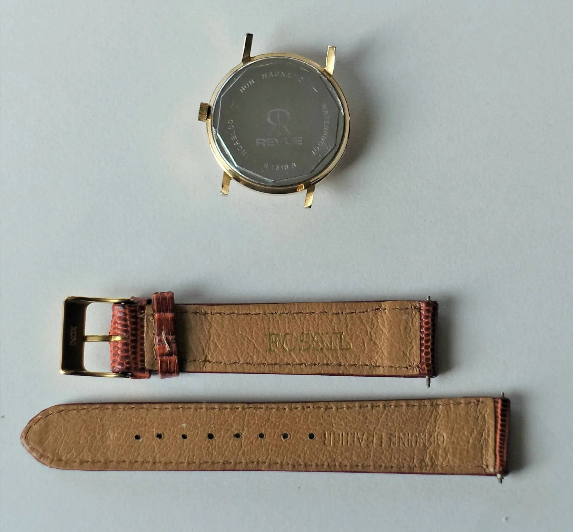 Uhrgehäuse goldfarben und Lederarmband Goldfarbenes Uhrgehäuse mit silberner Rückseite und braunes Lederarmband in zwei Teilen.