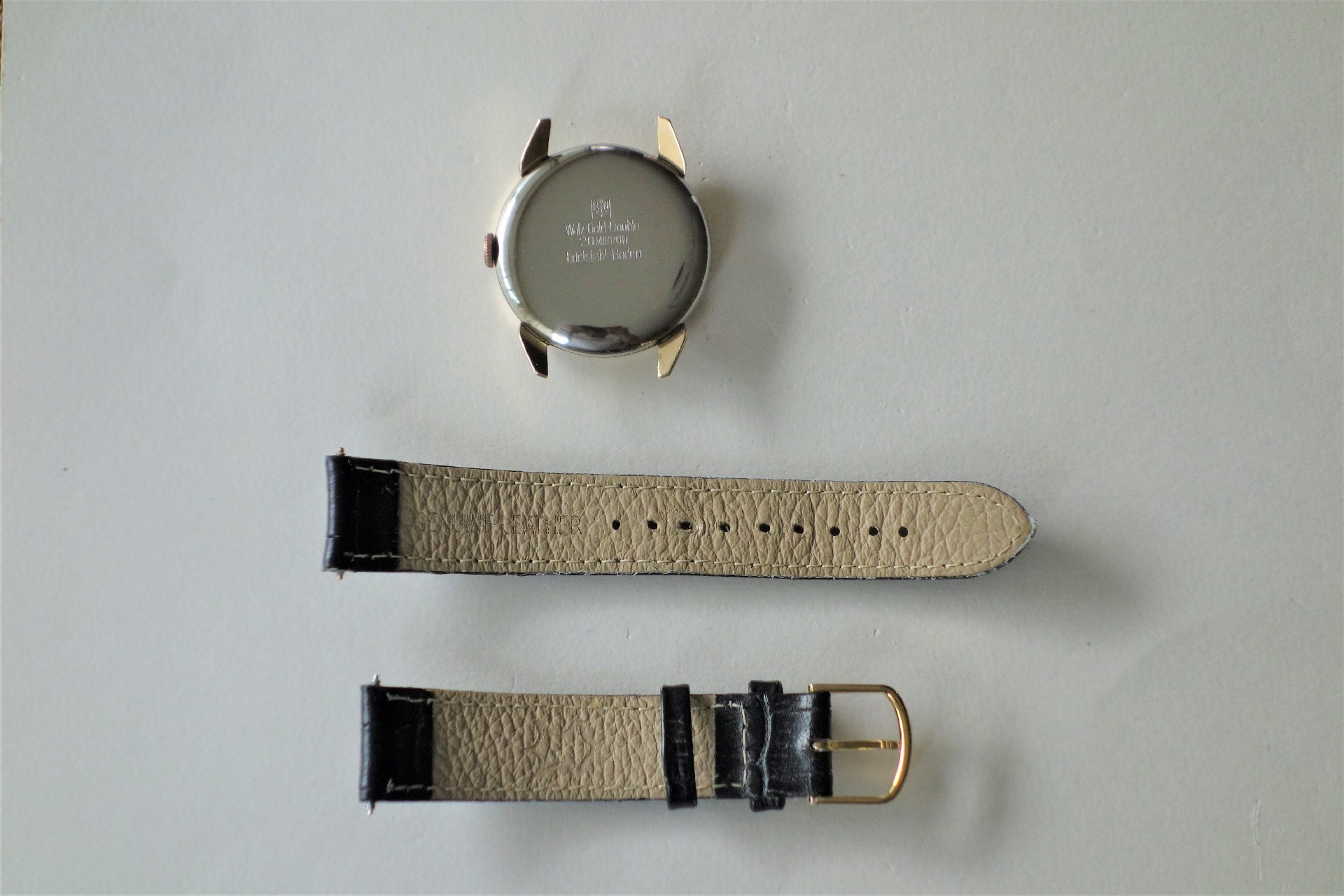 Silberfarbenes Uhrgehäuse und zweiteiliges beiges Lederarmband mit schwarzem Ende und goldfarbener Schließe.