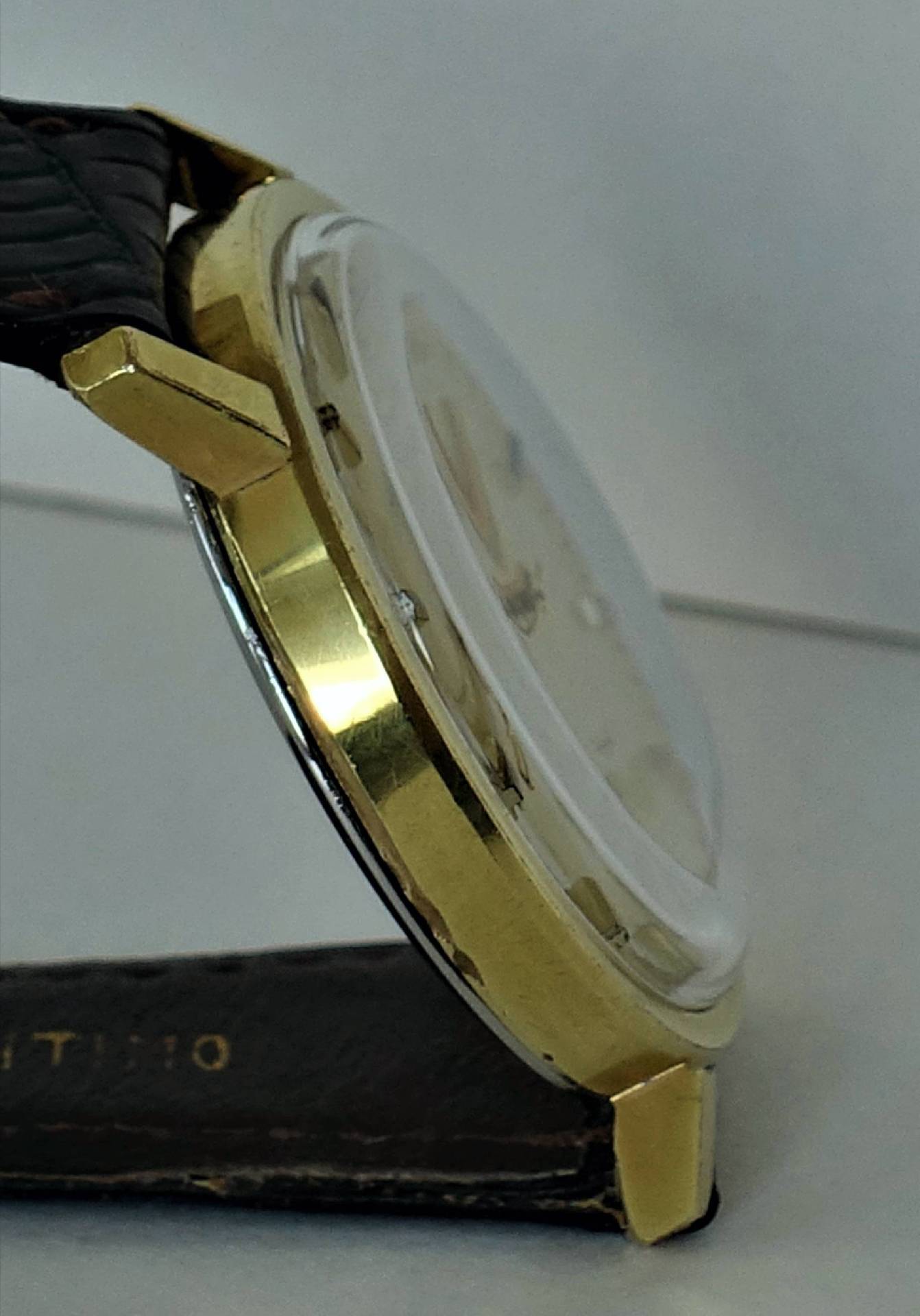 Seitliche Ansicht eines goldfarbenen Uhrgehäuses mit durchsichtigem Uhrglas und schwarzem Armband.