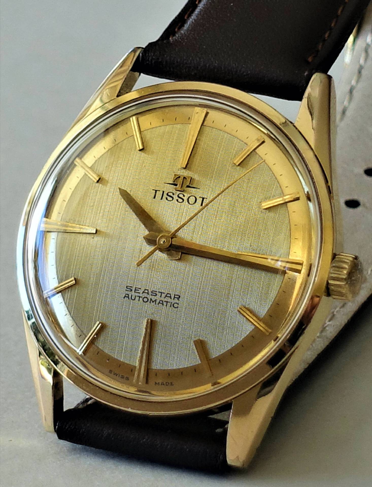 Goldfarbene Armbanduhr mit hellem Zifferblatt und braunem Armband, Modell Tissot Seastar Automatic.