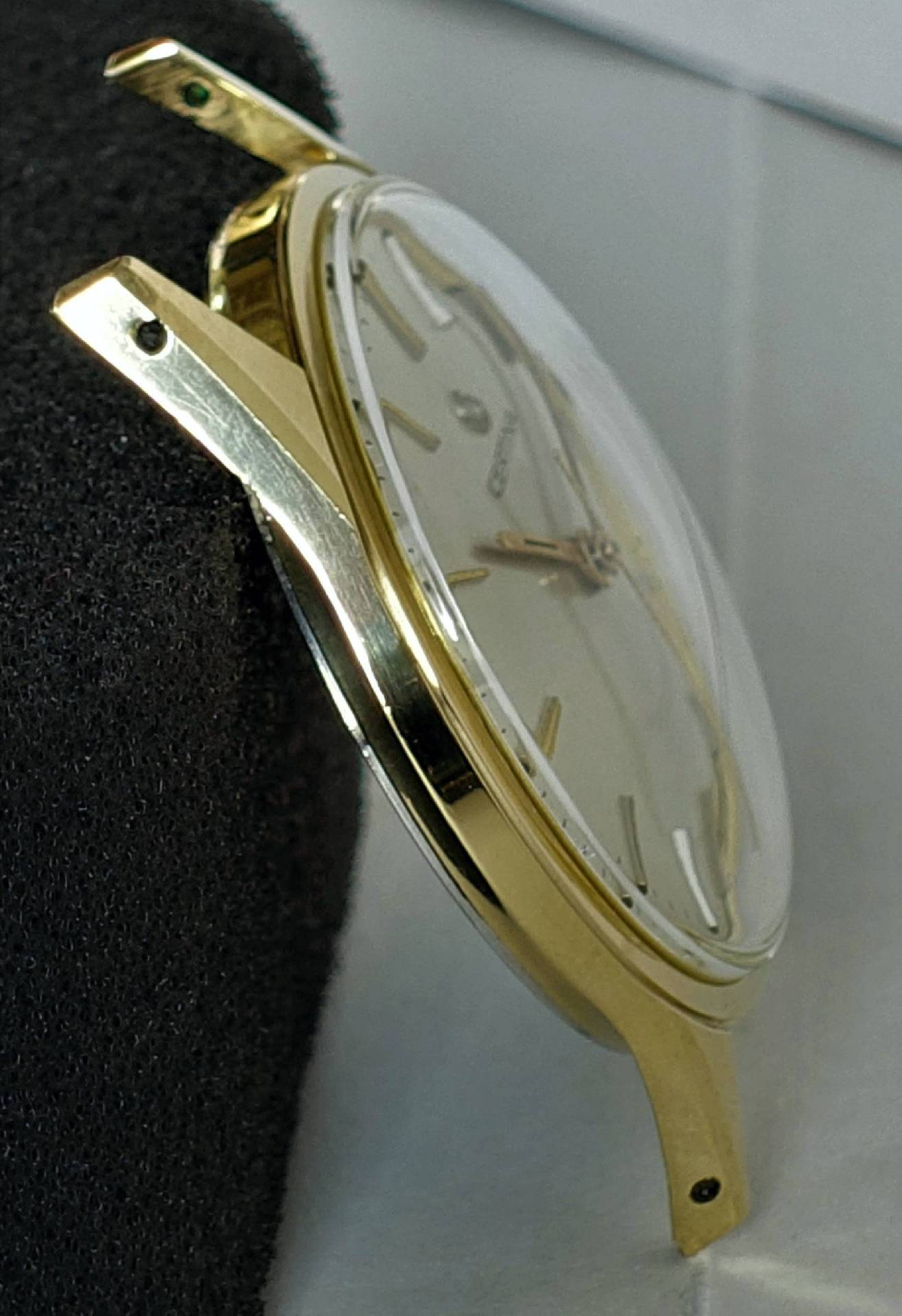 Flache Armbanduhr mit goldfarbenem Gehäuse und hellem Zifferblatt.