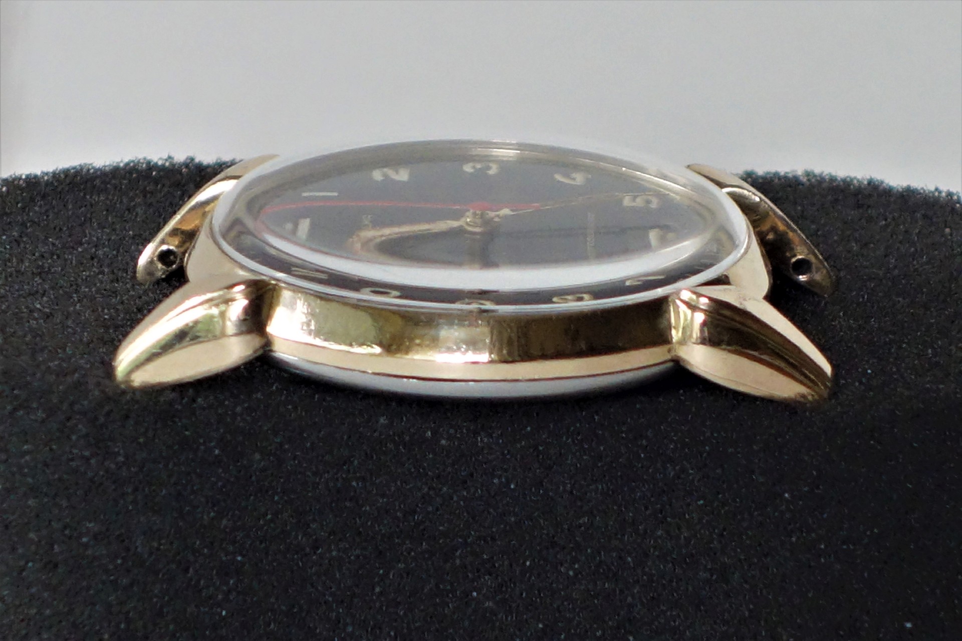 Goldfarbenes Uhrgehäuse mit schwarzem Zifferblatt und Glasabdeckung, ohne Armband.
