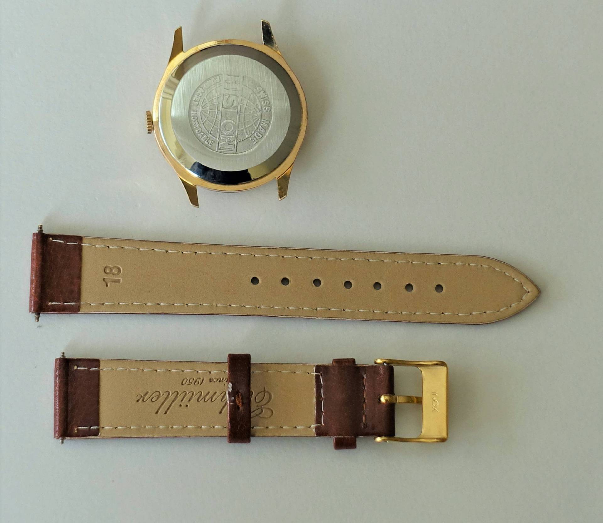 Rückseite eines goldfarbenen Uhrgehäuses mit silberner Bodenplatte und einem zweiteiligen braunen Lederarmband mit heller Unterseite.