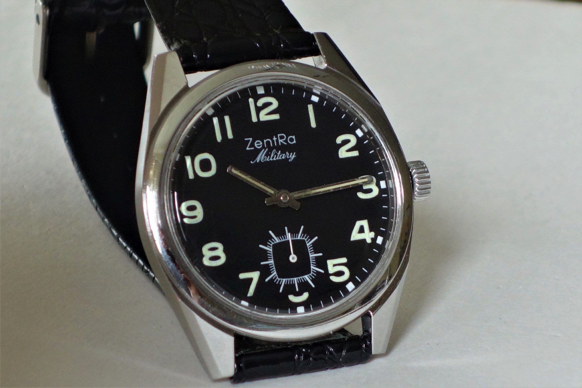 Schwarze Armbanduhr mit hellem Zifferblatt und schwarzem Armband.