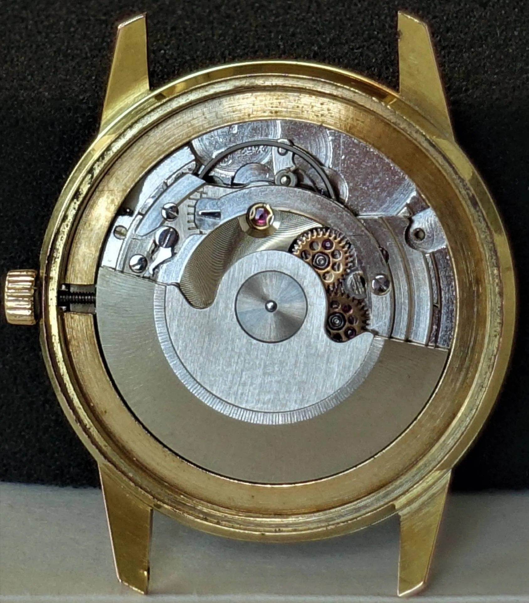 Eine Armbanduhr mit goldfarbenem Gehäuse zeigt ihr silbernes mechanisches Uhrwerk mit sichtbaren Zahnrädern und Rotor.