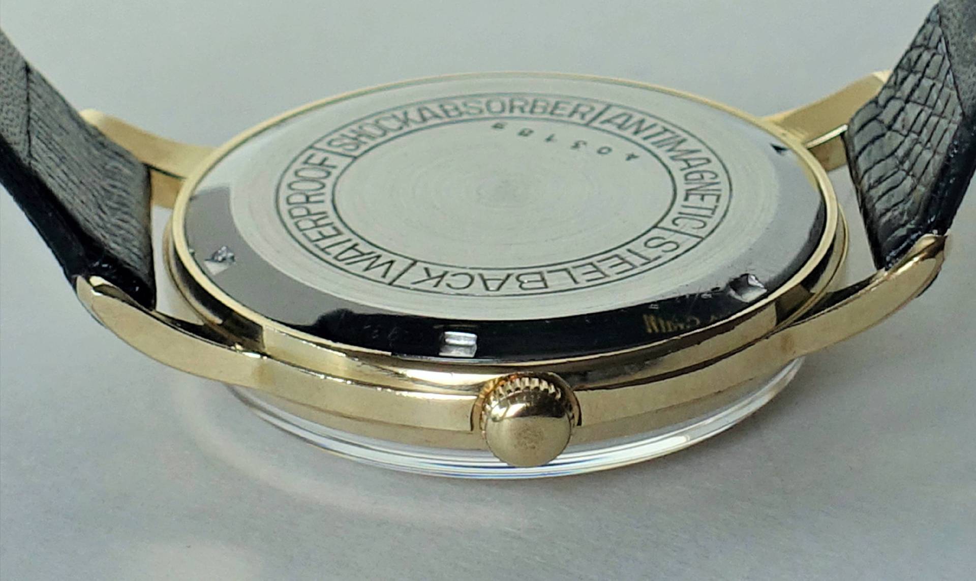 Rückseite einer goldfarbenen Armbanduhr mit schwarzem Armband und silberfarbenem Gehäuseboden.