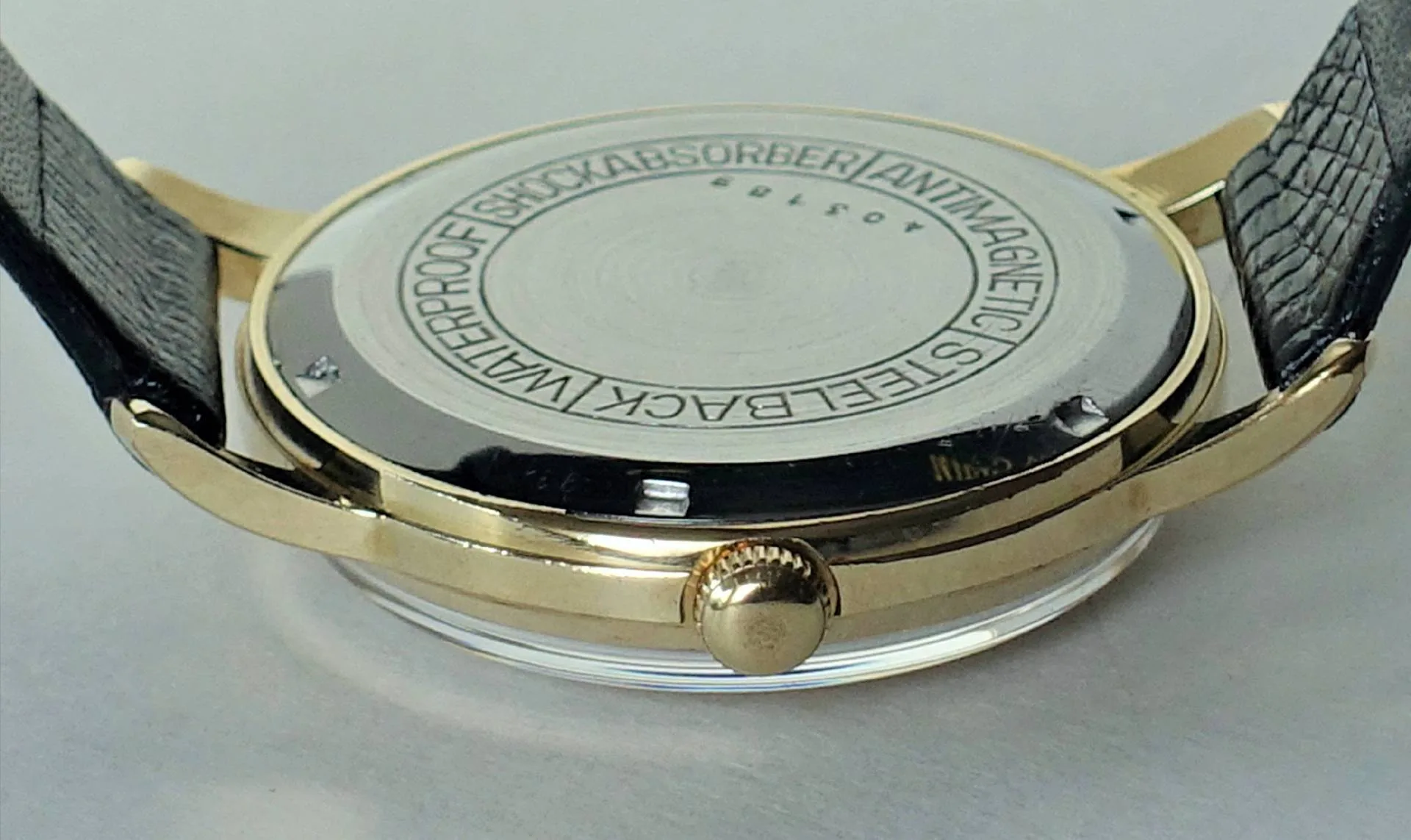 Rückseite einer goldfarbenen Armbanduhr mit schwarzem Armband und silberfarbenem Gehäuseboden.