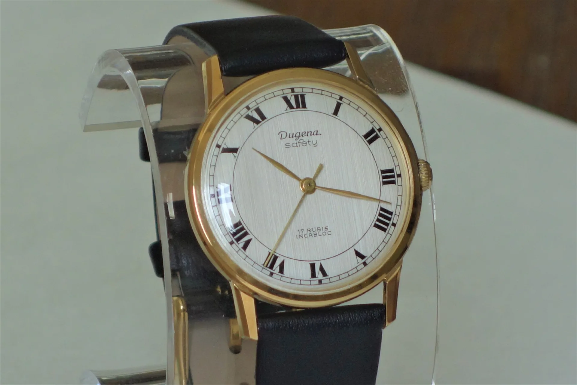 Klassische Armbanduhr mit goldfarbenem Gehäuse, hellem Zifferblatt und schwarzem Lederarmband.