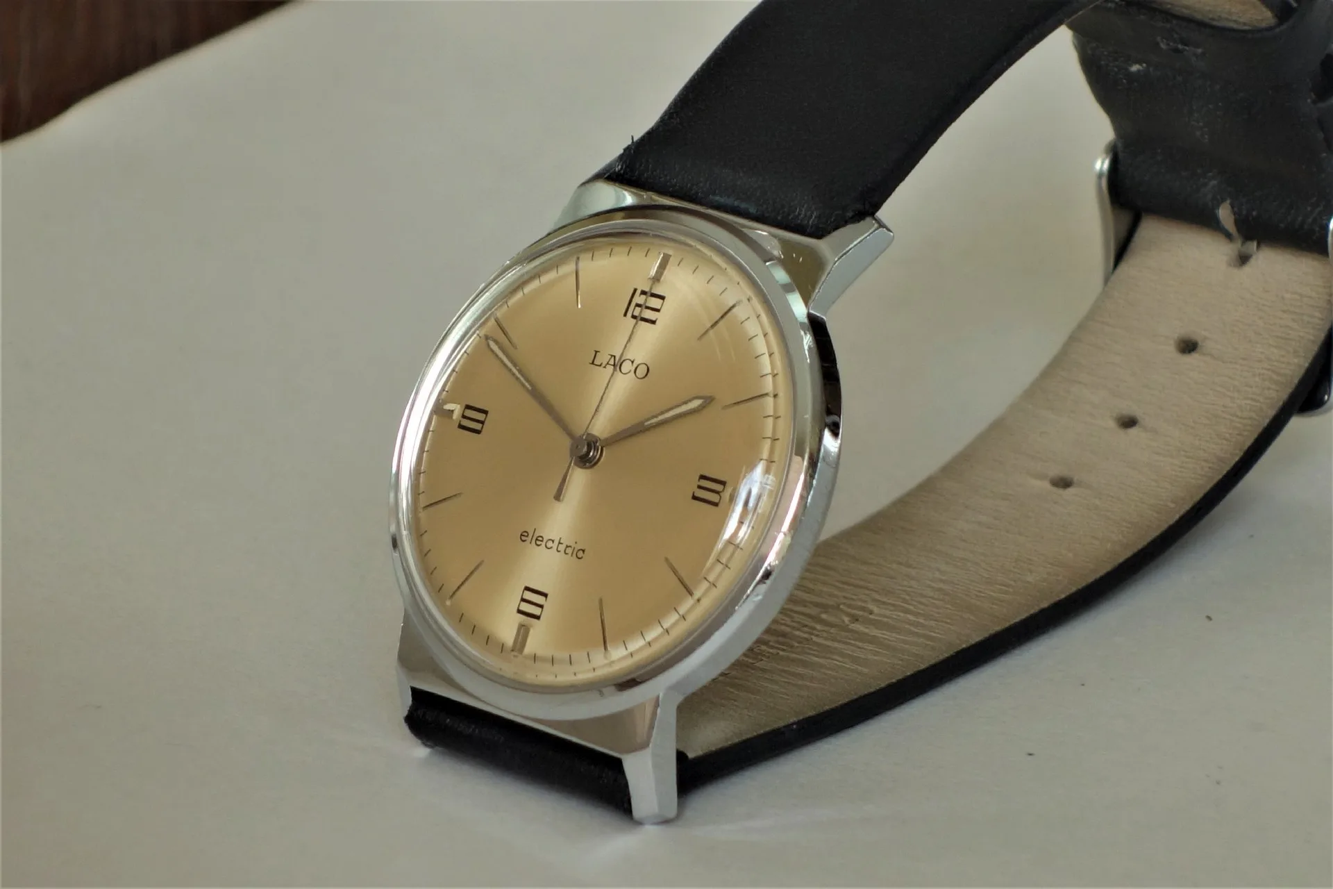 Analoge Armbanduhr mit hellem Zifferblatt und schwarzem Lederarmband.