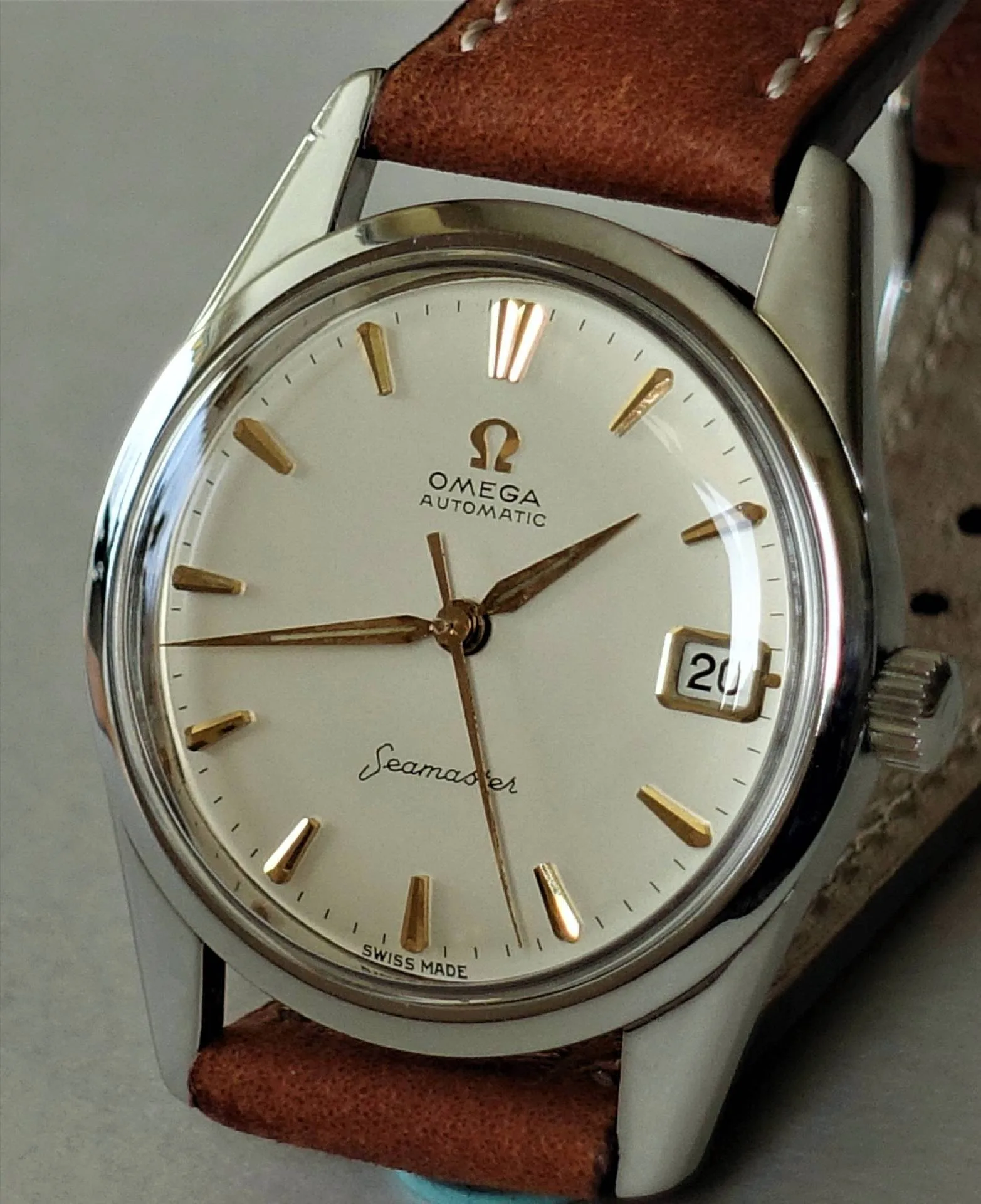 Omega Seamaster Armbanduhr Silberne Armbanduhr mit weißem Zifferblatt, goldfarbenen Indizes und braunem Lederarmband.