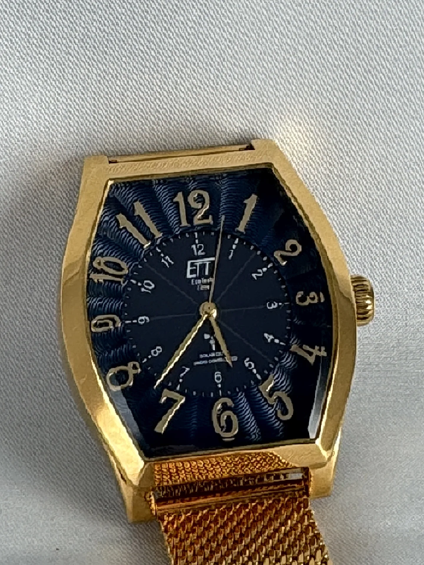 Goldfarbene Armbanduhr mit tonneauförmigem Gehäuse, blauem Zifferblatt und goldfarbenem Milanaise-Armband.
