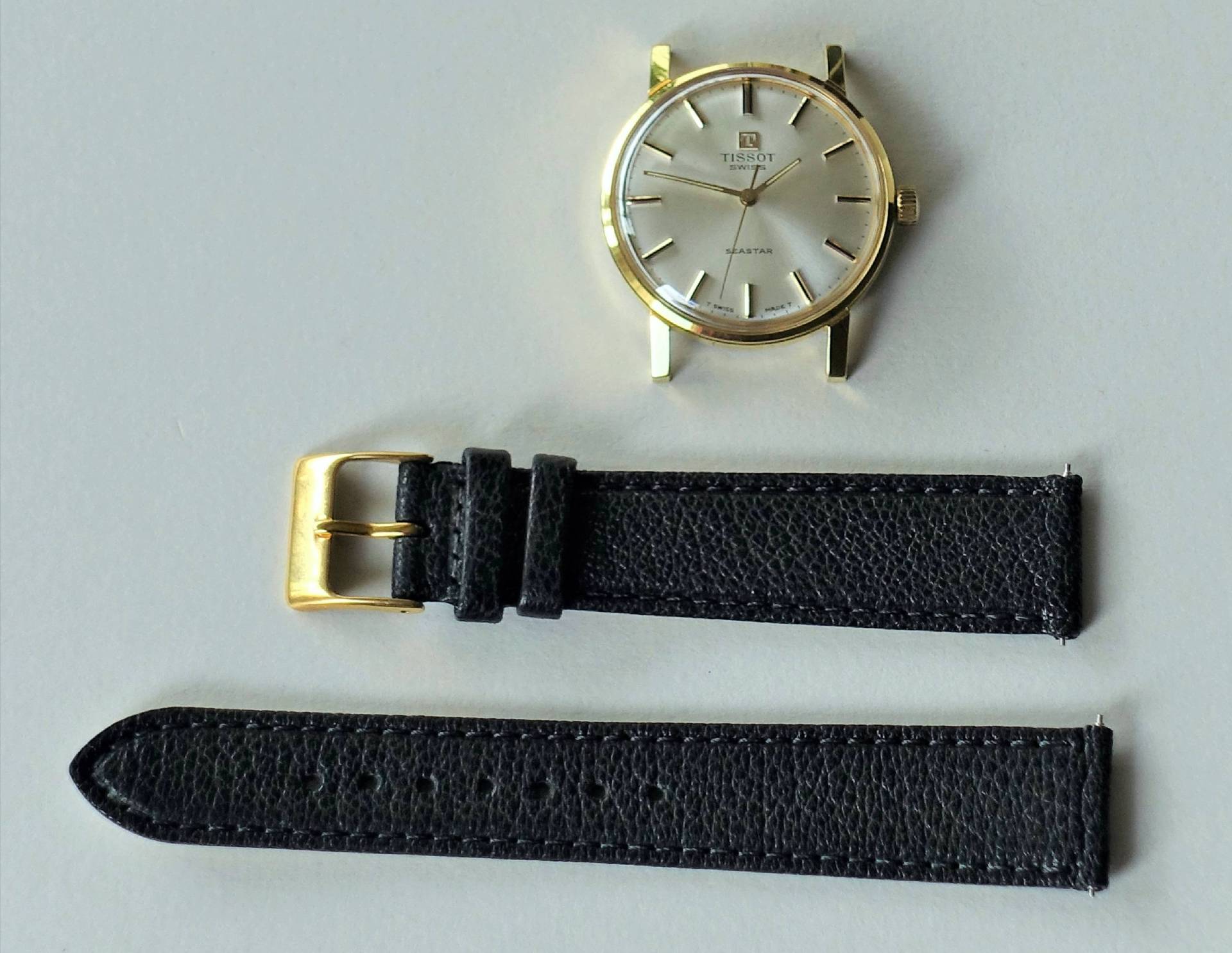 Goldfarbene Armbanduhr mit schwarzem Lederarmband, bestehend aus Uhrgehäuse und zwei Armbandteilen.