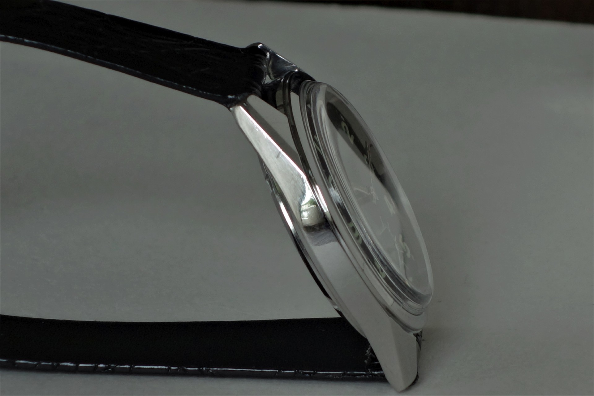 Armbanduhr mit silberfarbenem Gehäuse und schwarzem Armband in Seitenansicht.