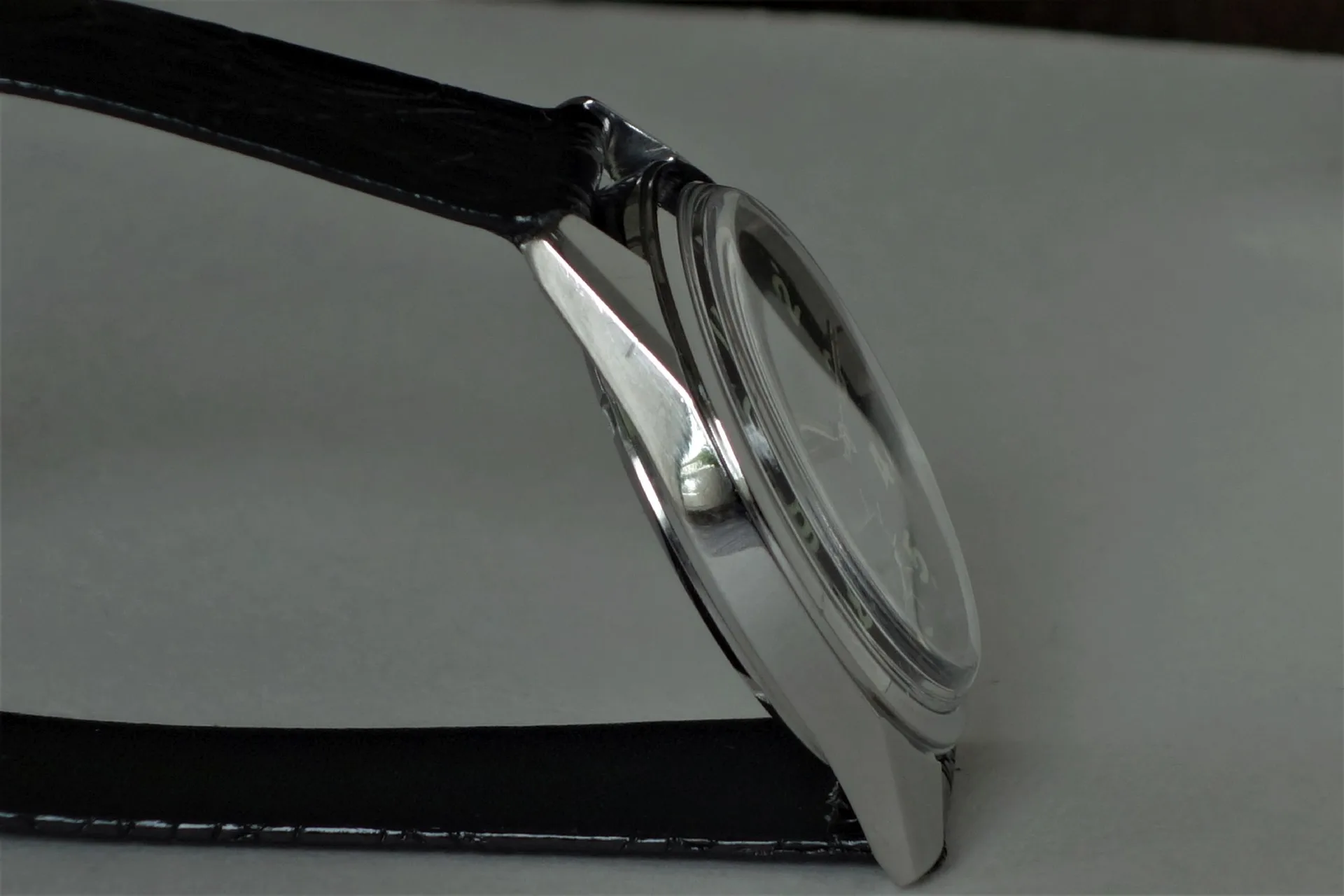 Uhr mit schwarzem Armband Armbanduhr mit silberfarbenem Gehäuse und schwarzem Armband in Seitenansicht.