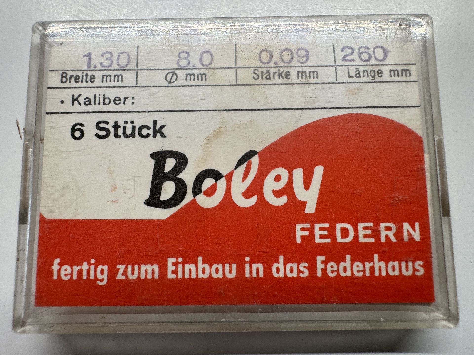 Verpackung mit sechs Federn für Uhrwerke, geeignet zum Einbau in das Federhaus.