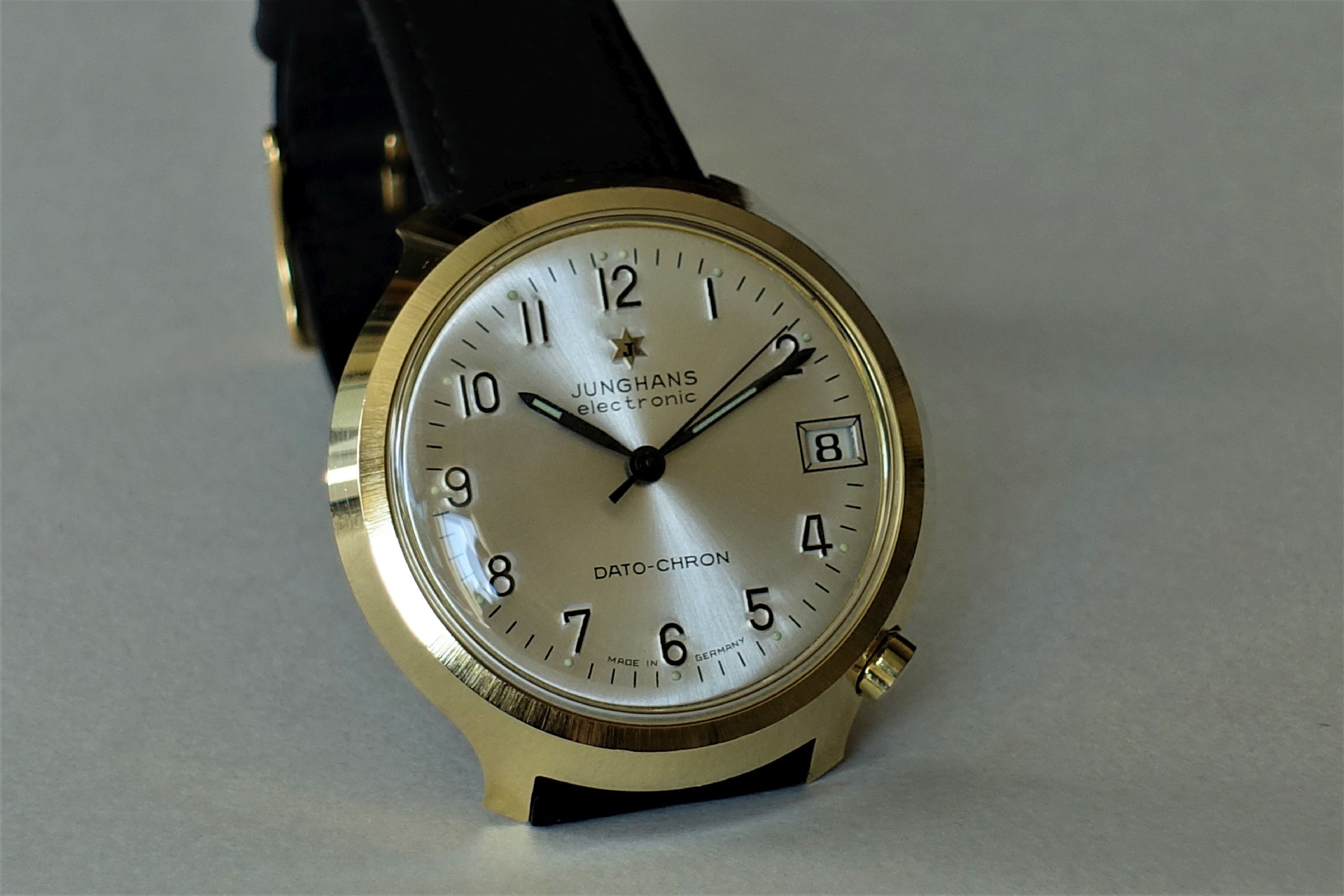 Analoge Armbanduhr mit goldfarbenem Gehäuse, hellem Zifferblatt und schwarzem Lederarmband.