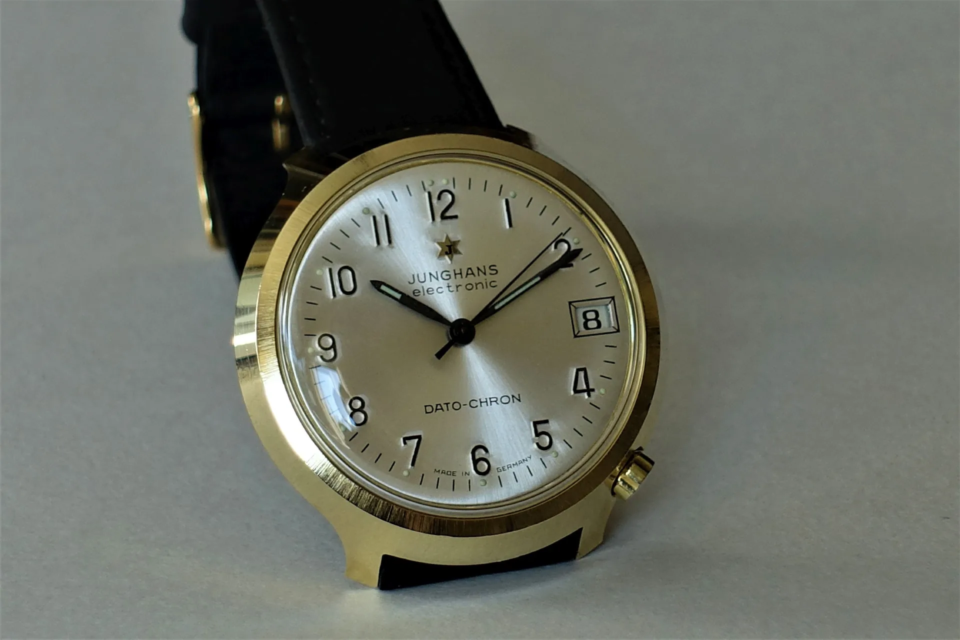 Analoge Armbanduhr mit goldfarbenem Gehäuse, hellem Zifferblatt und schwarzem Lederarmband.