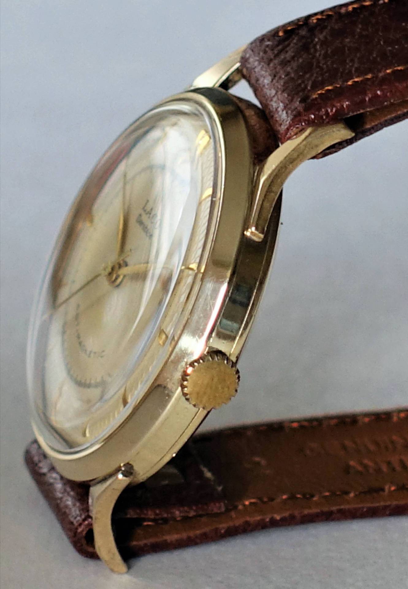 Goldfarbene Armbanduhr mit braunem Lederarmband und hellem Zifferblatt.