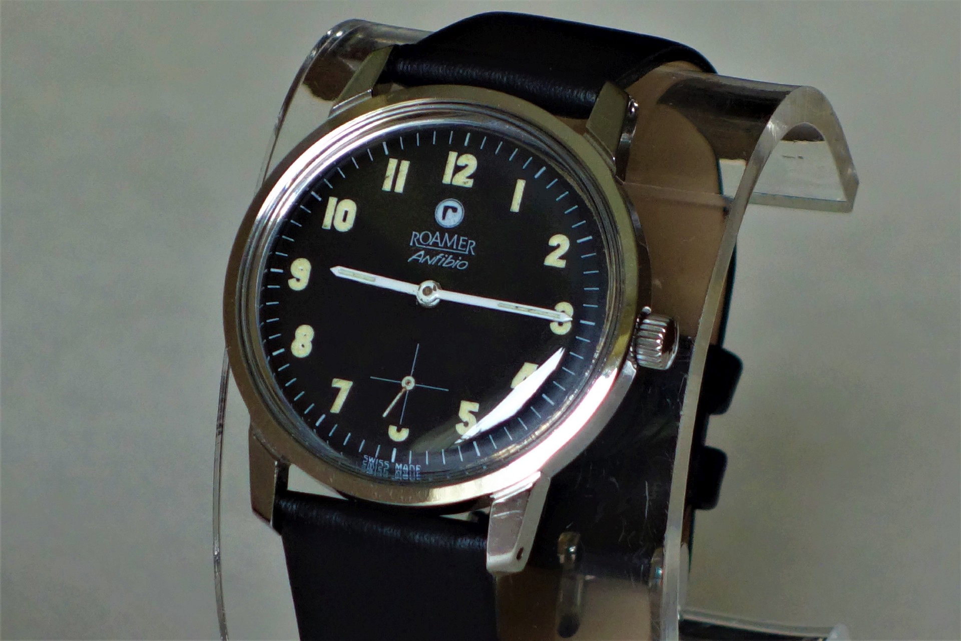 Schwarze Armbanduhr mit hellem Zifferblatt und Lederarmband.