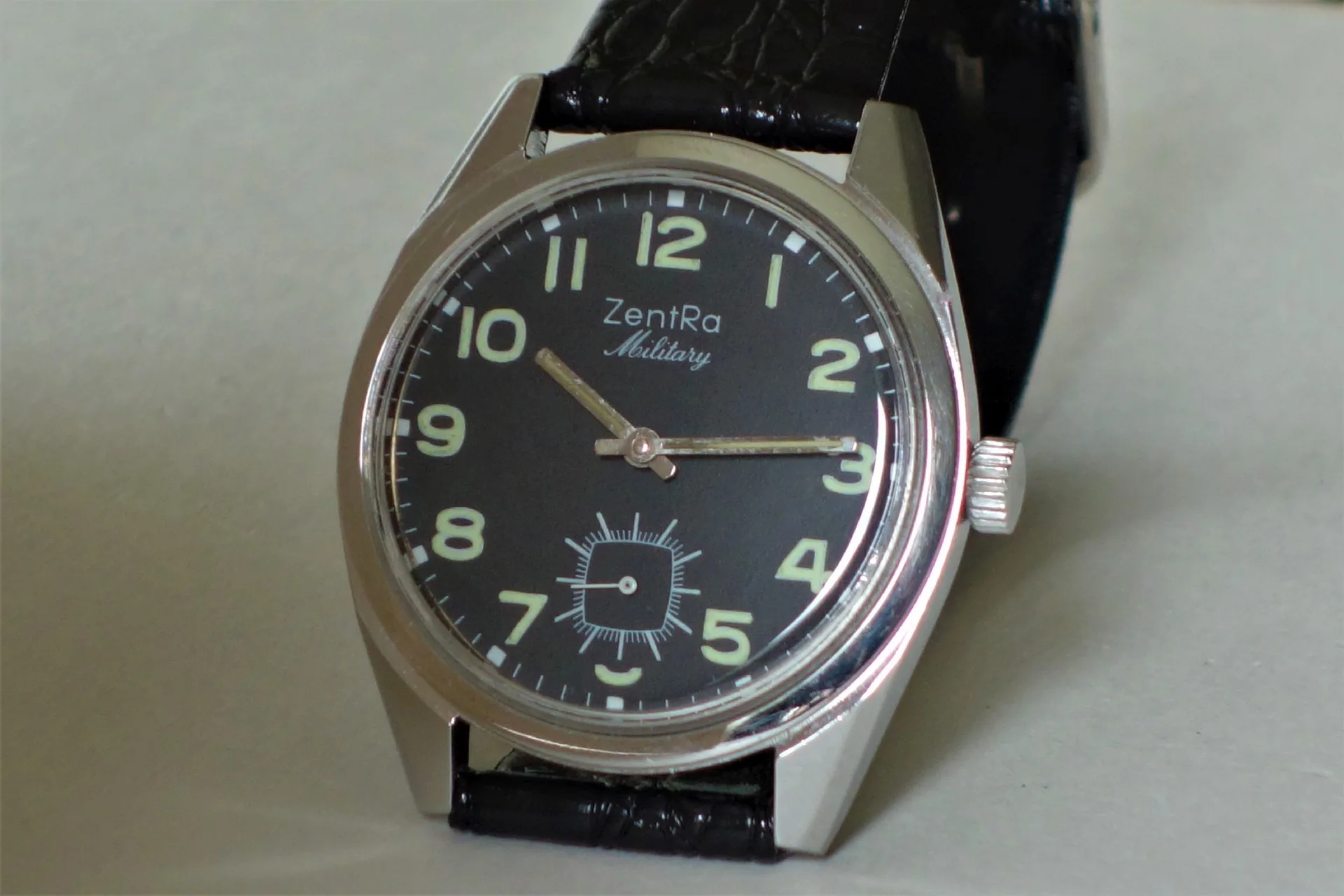 Schwarze Armbanduhr mit Leuchtziffern und schwarzem Armband.