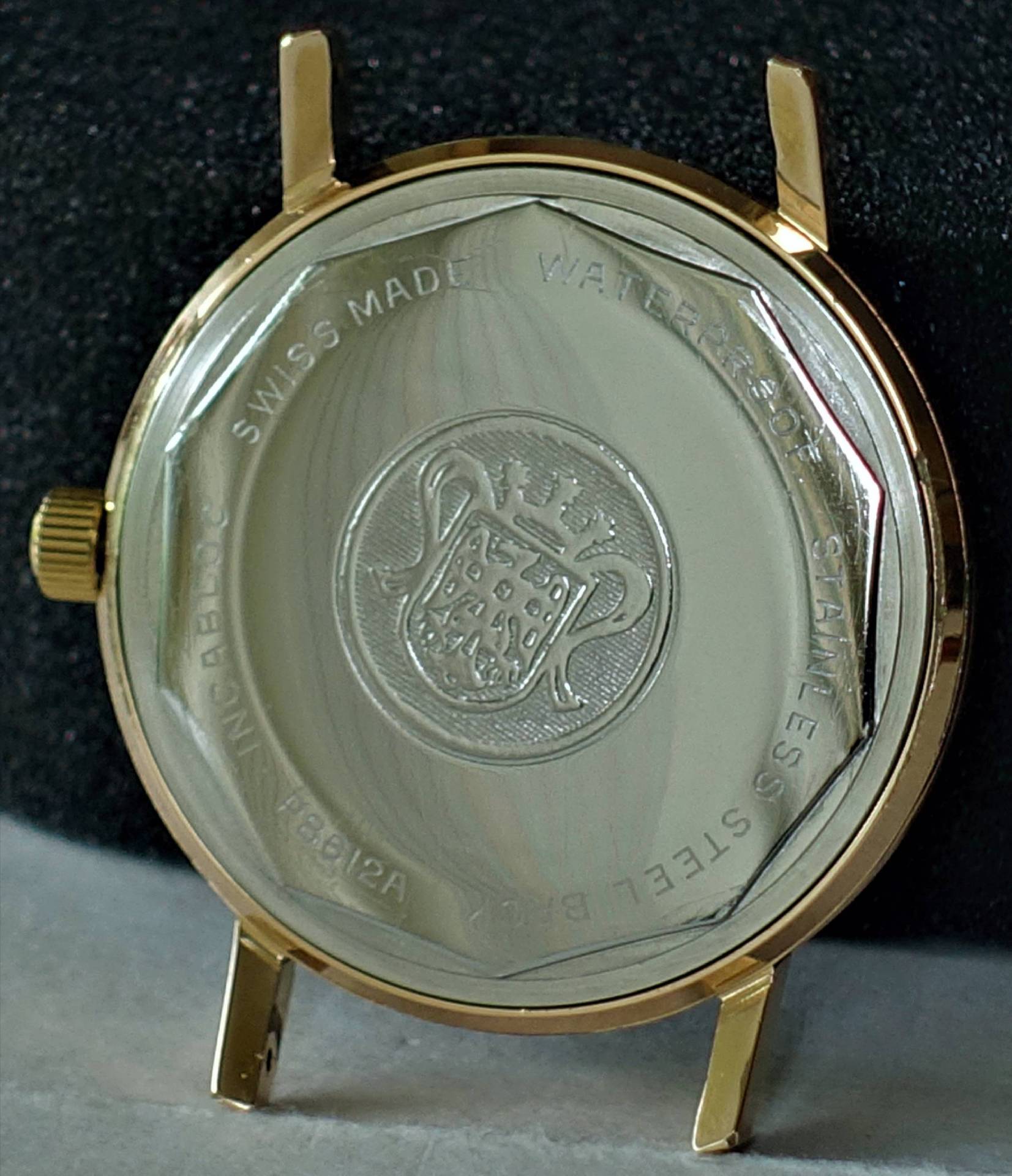 Goldfarbenes Uhrgehäuse mit silberfarbener Rückseite und Gravur eines Wappens.